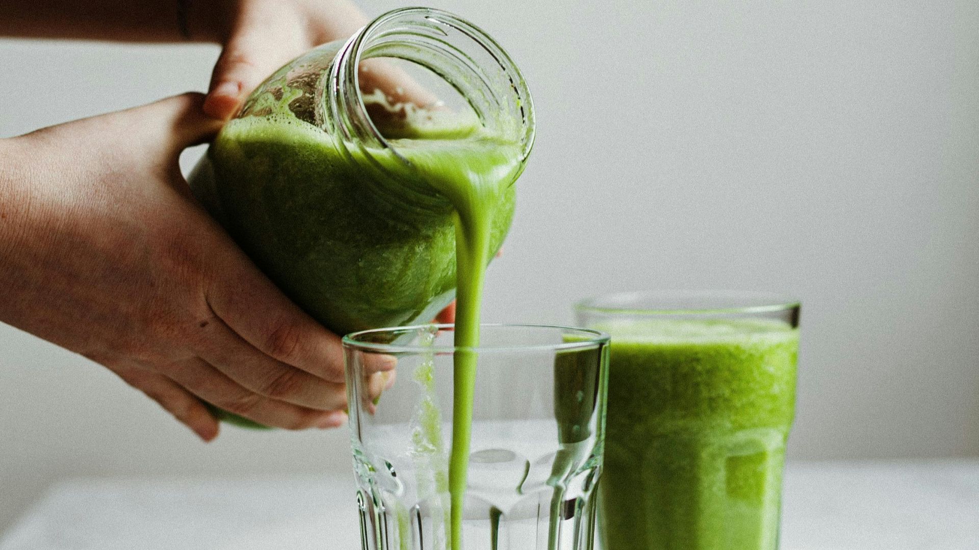 person holding clear drinking glass with green liquid