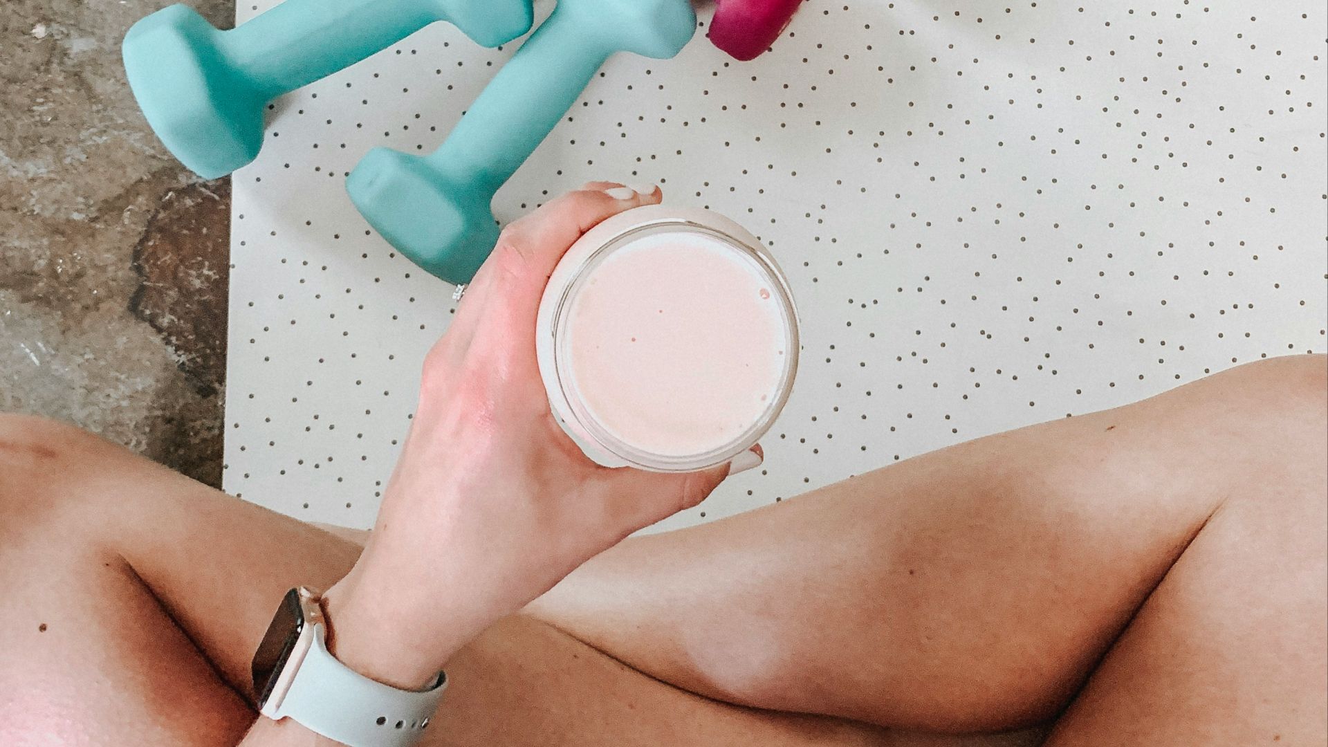 person holding white liquid filled cup above two pairs of dumbbells
