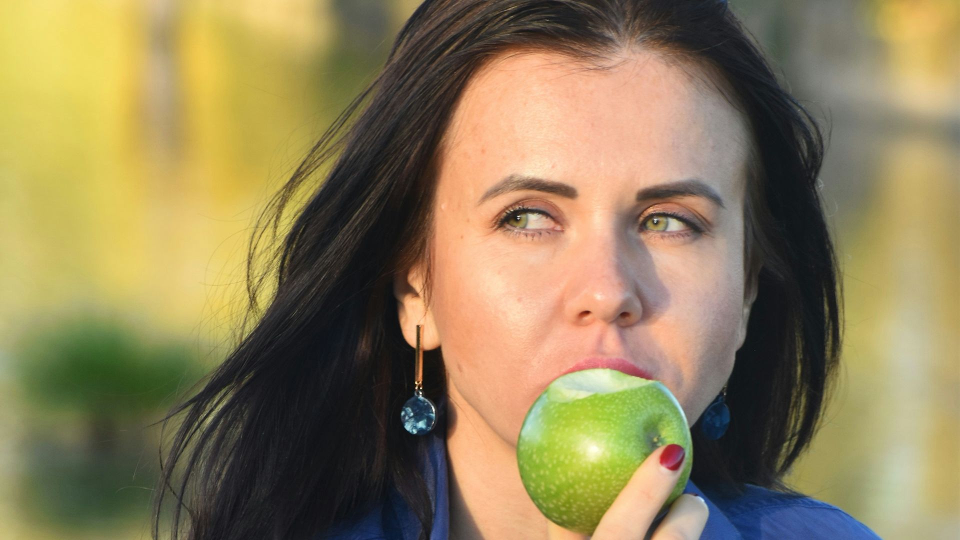 a woman in a blue shirt eating an apple