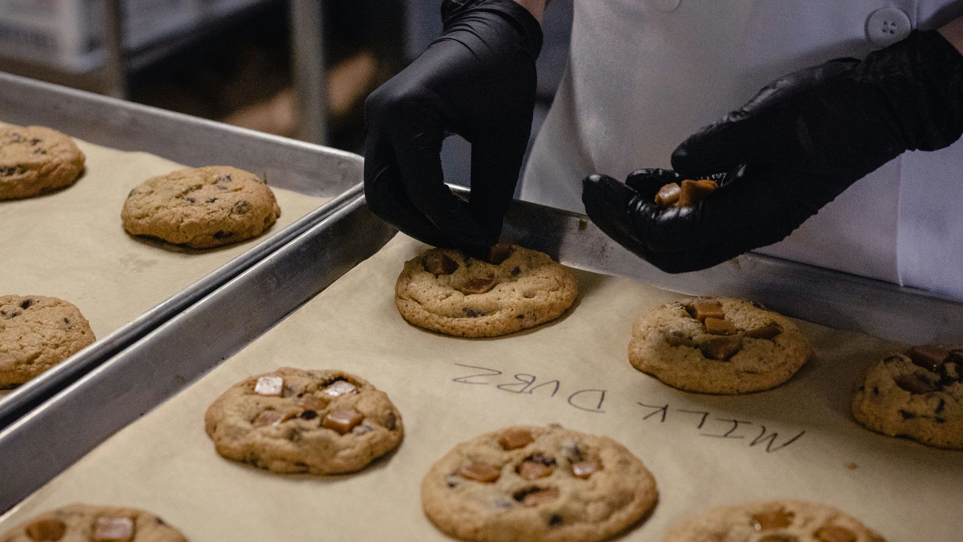 person in white apron holding brown cookies