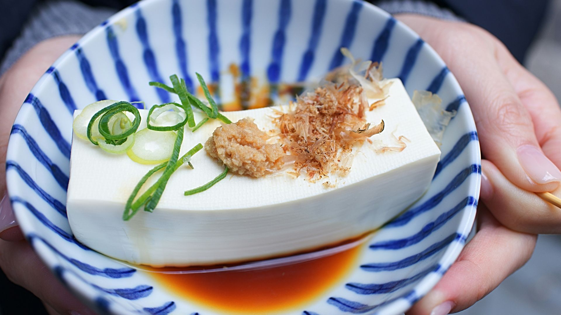 person holding white and blue ceramic plate with rice and sliced cucumber