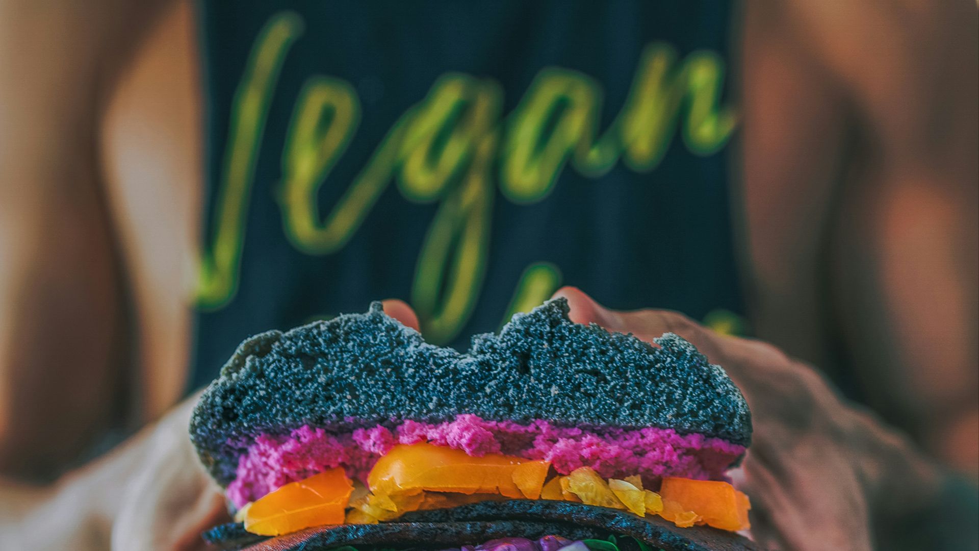 person holding meat sandwich with sliced tomatoes, onions, and grilled meat
