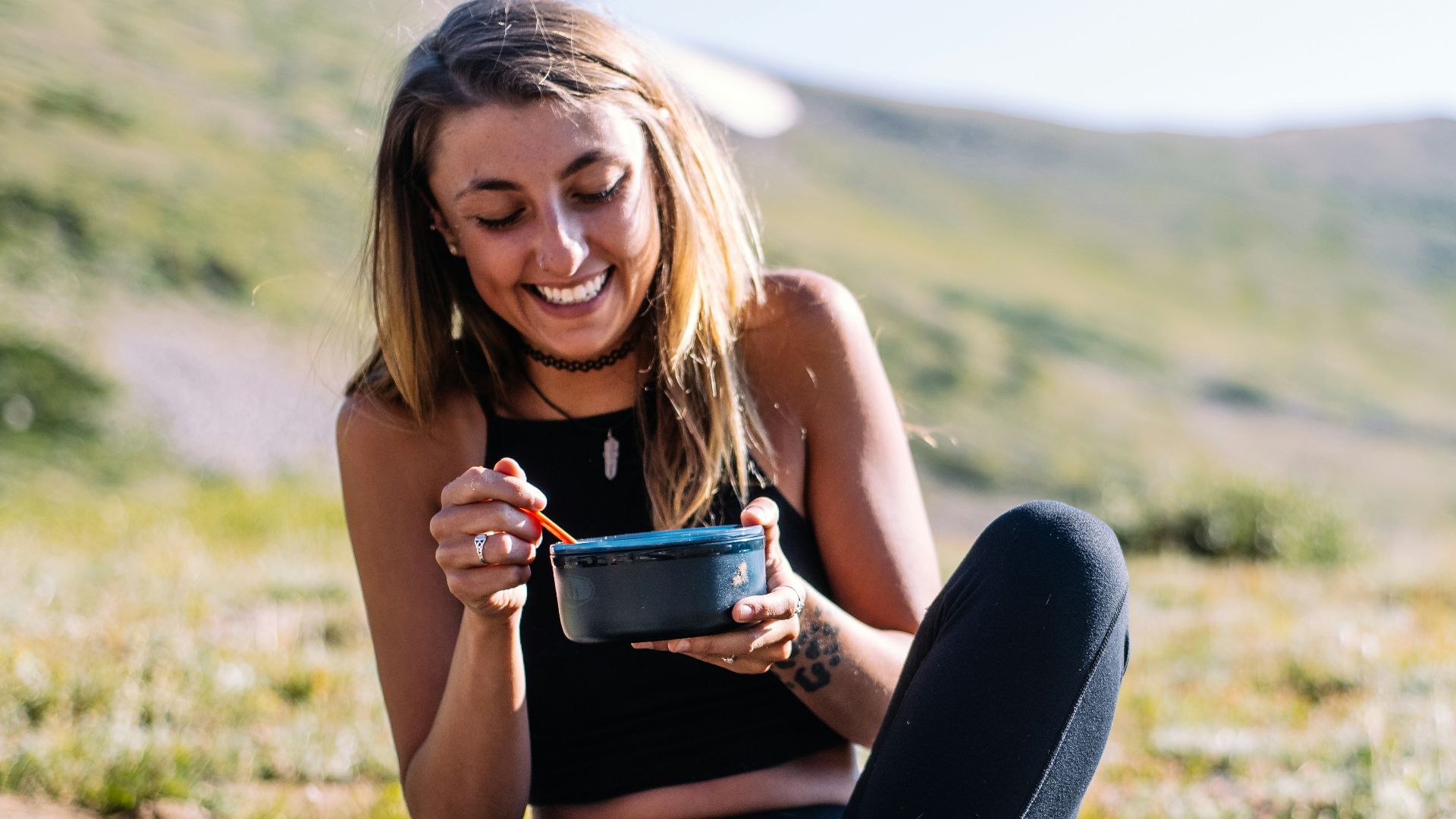 woman in black tank top and black pants sitting on ground holding blue ceramic mug during