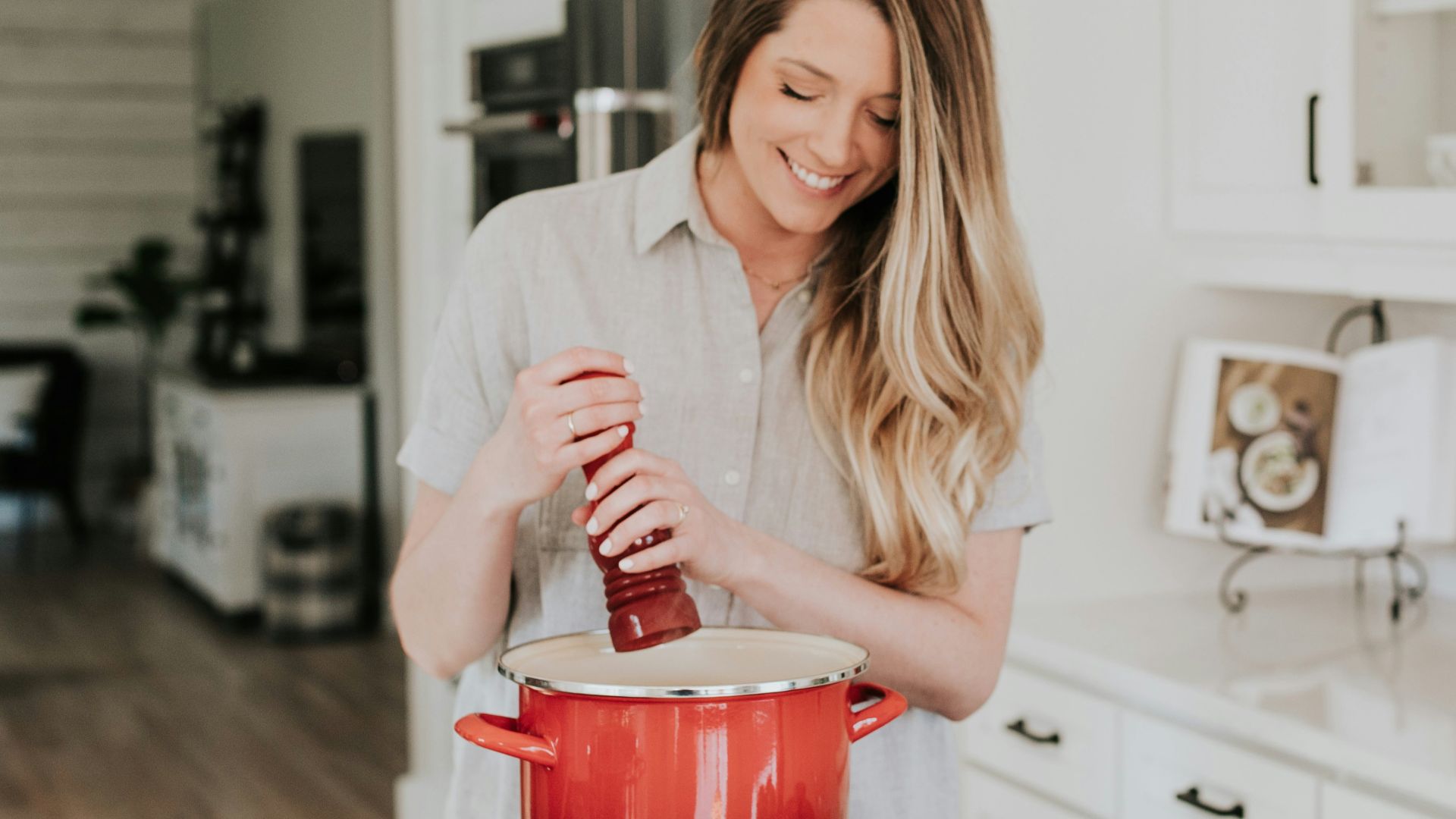 smiling woman standing and putting pepper on stock pot