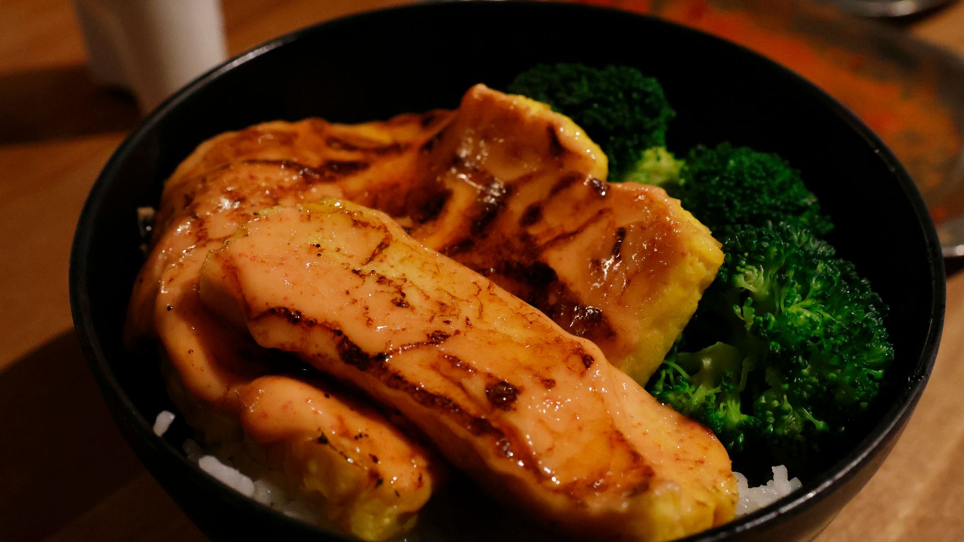 a bowl filled with meat and broccoli on top of a wooden table