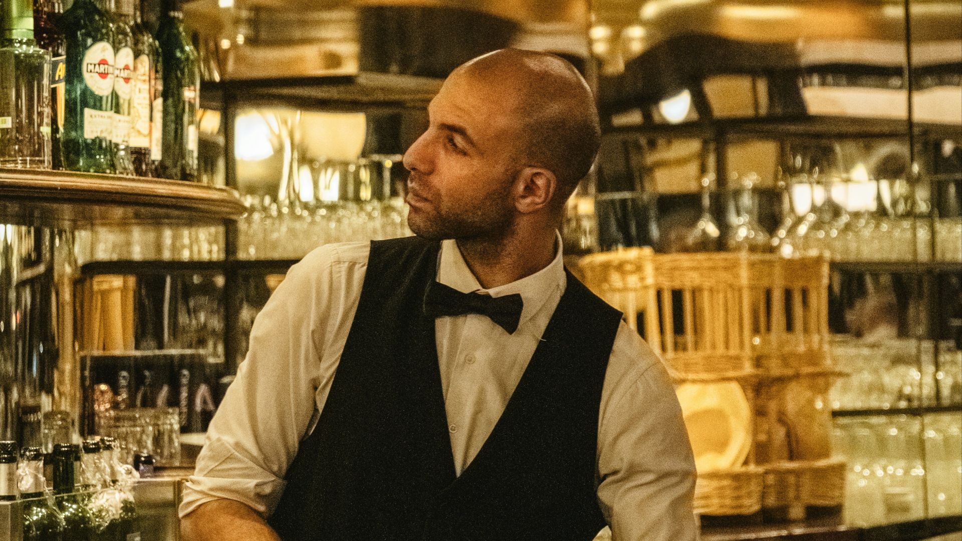 a man wearing a bow tie standing in front of a bar