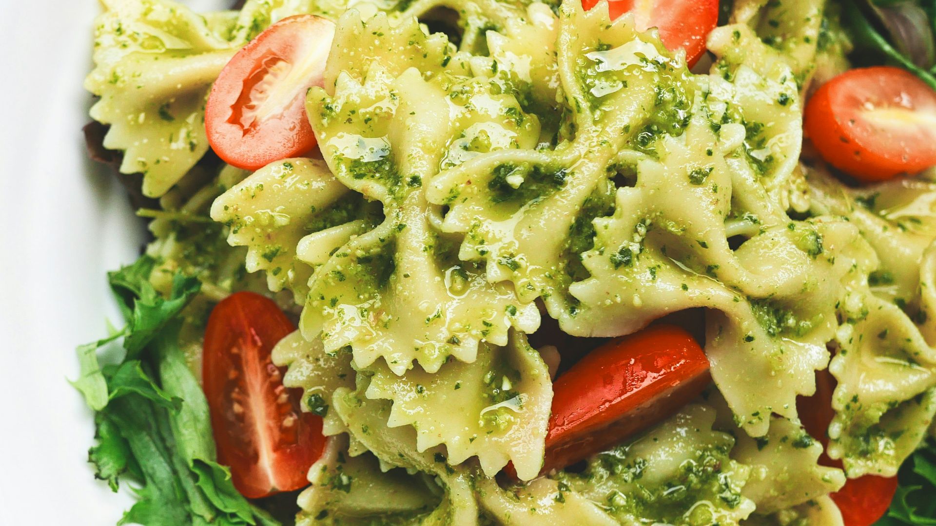 Pesto pasta with sliced tomatoes served on white ceramic plate