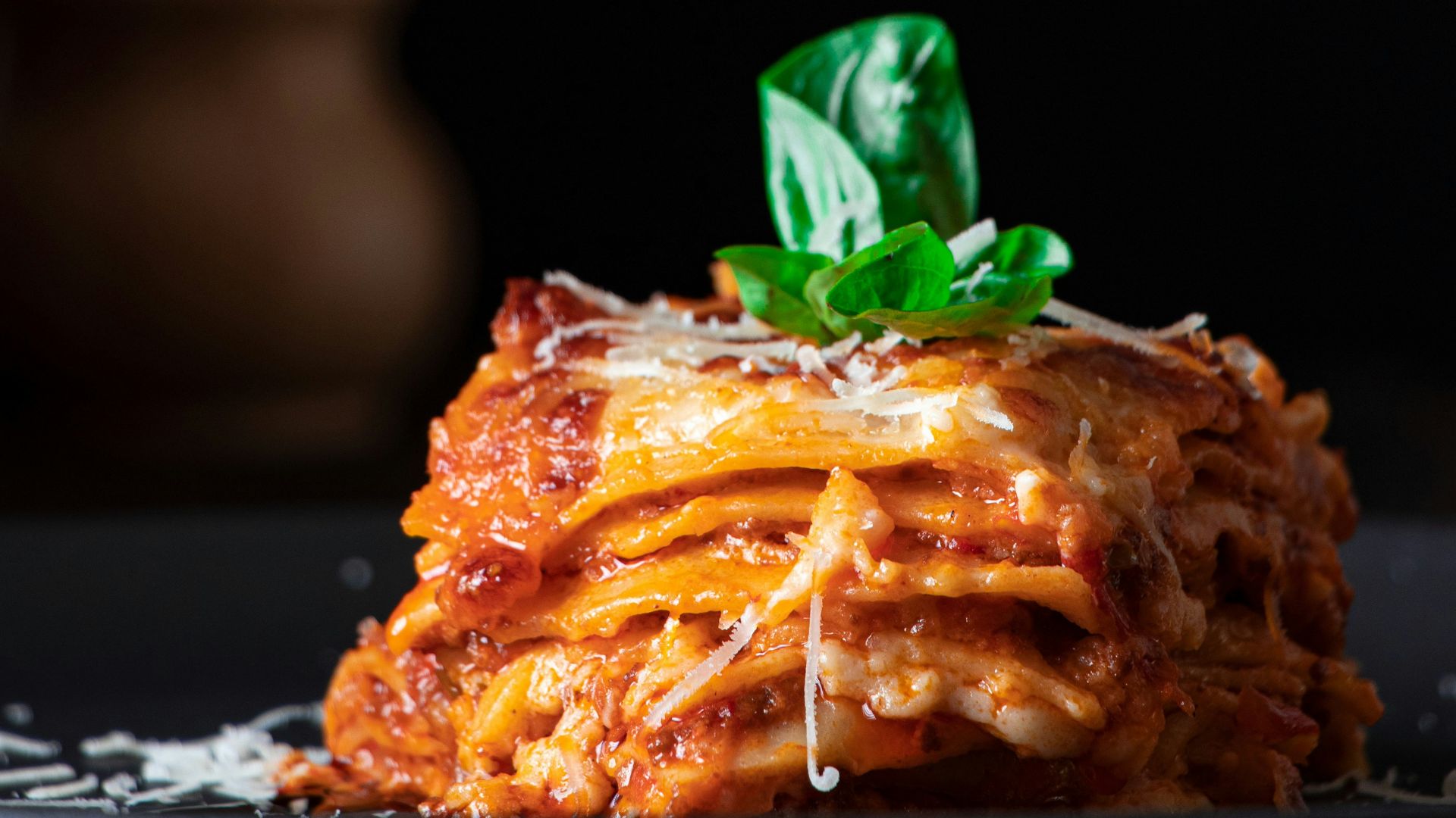 A black plate topped with lasagna covered in sauce and cheese