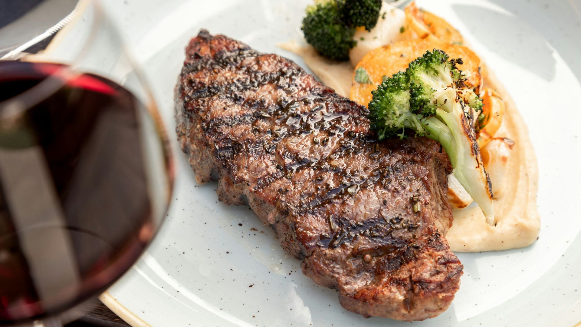a white plate topped with meat and veggies next to a glass of wine