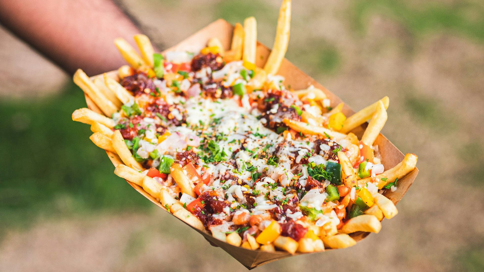 a person holding a tray of fries with cheese and other toppings