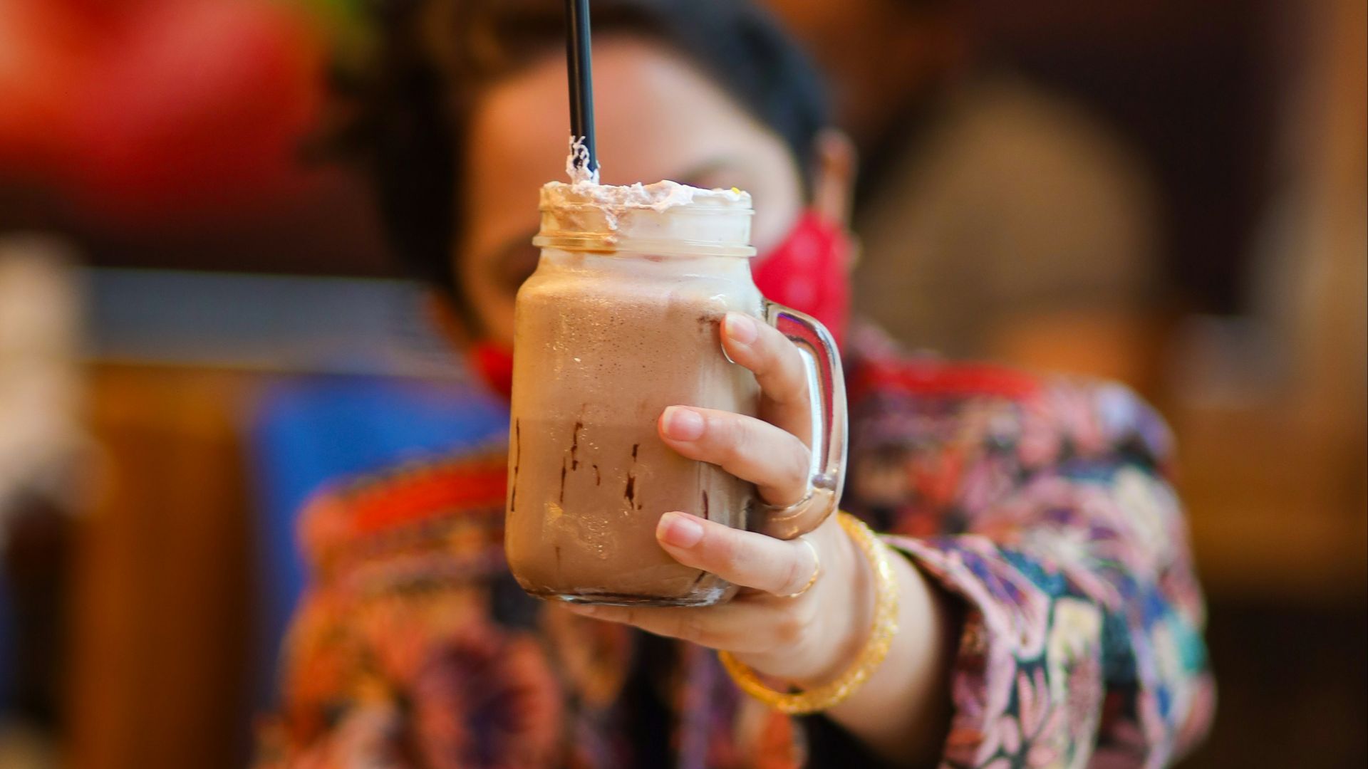 a woman holding a drink over a plate of food
