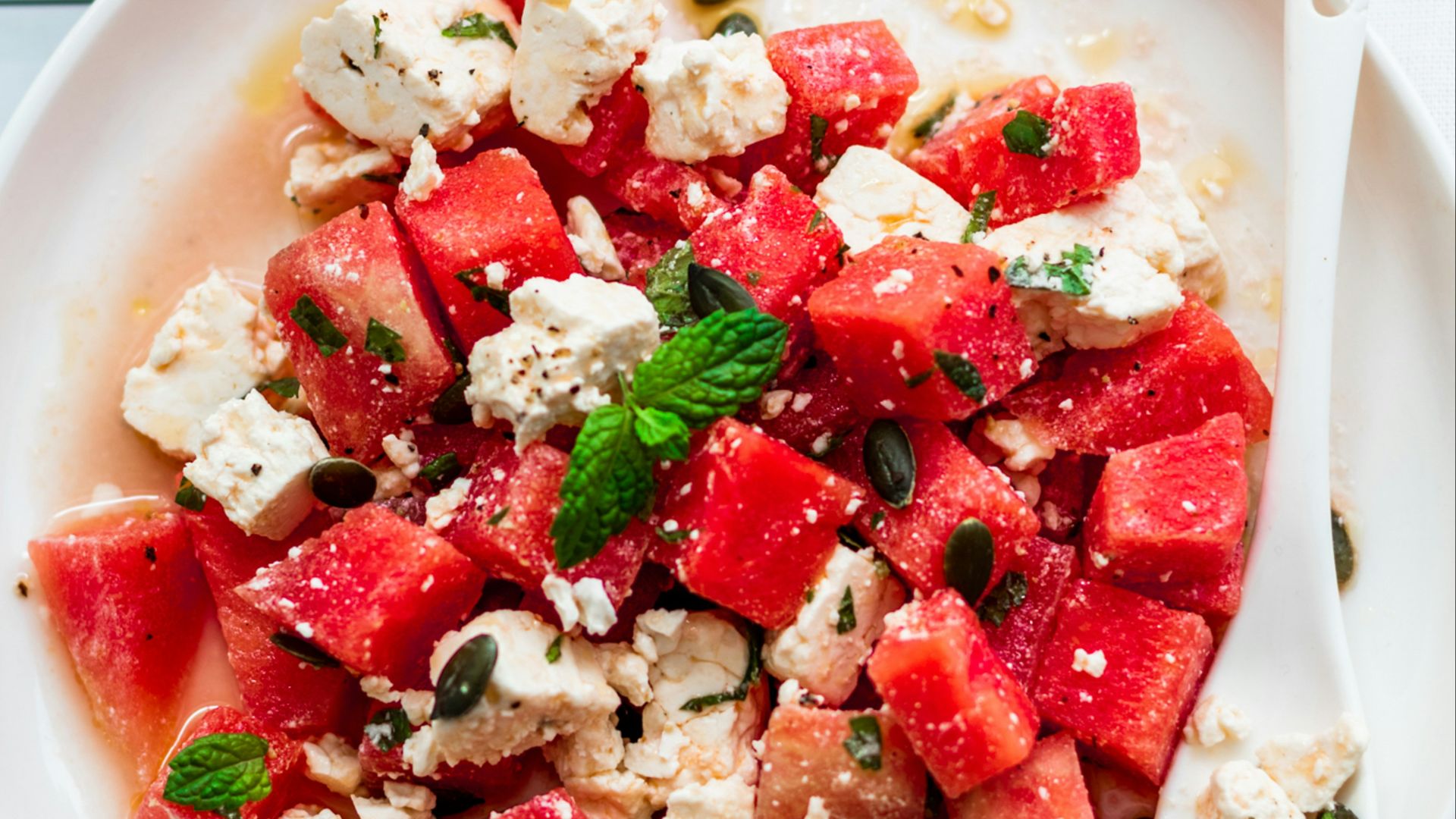 a plate of watermelon and feta salad next to a glass of water