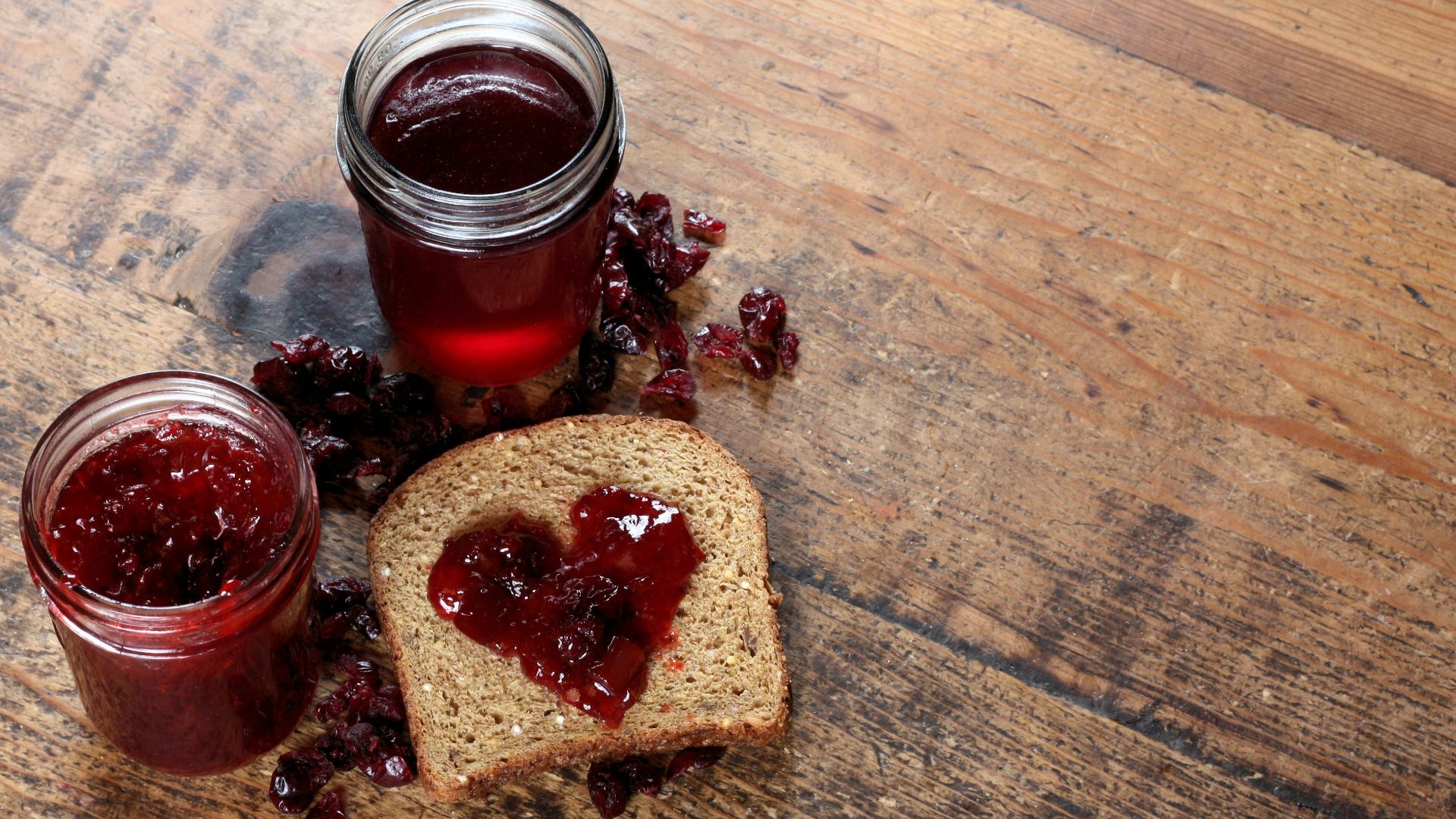 two jars of jam sit next to a piece of bread