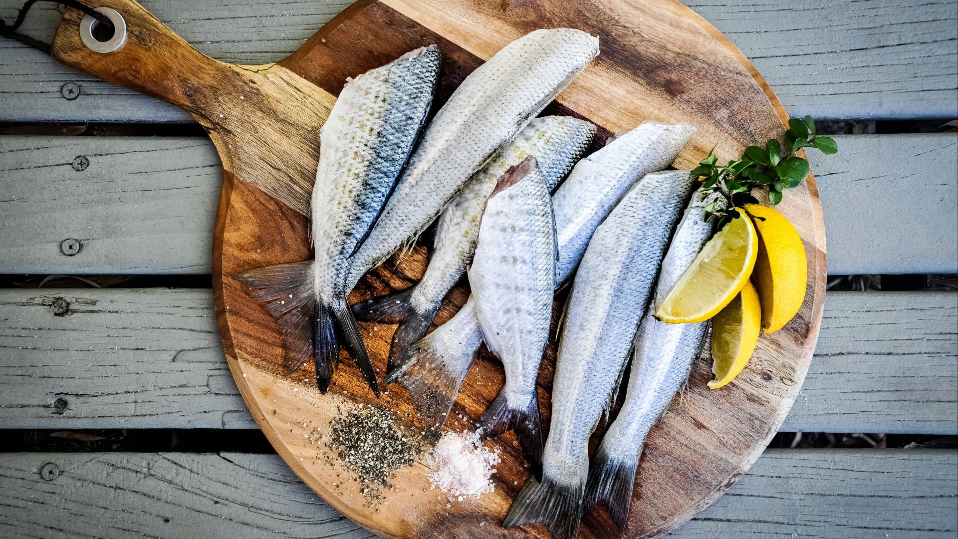 headless fishes with sliced of lemons on brown wooden chopping board