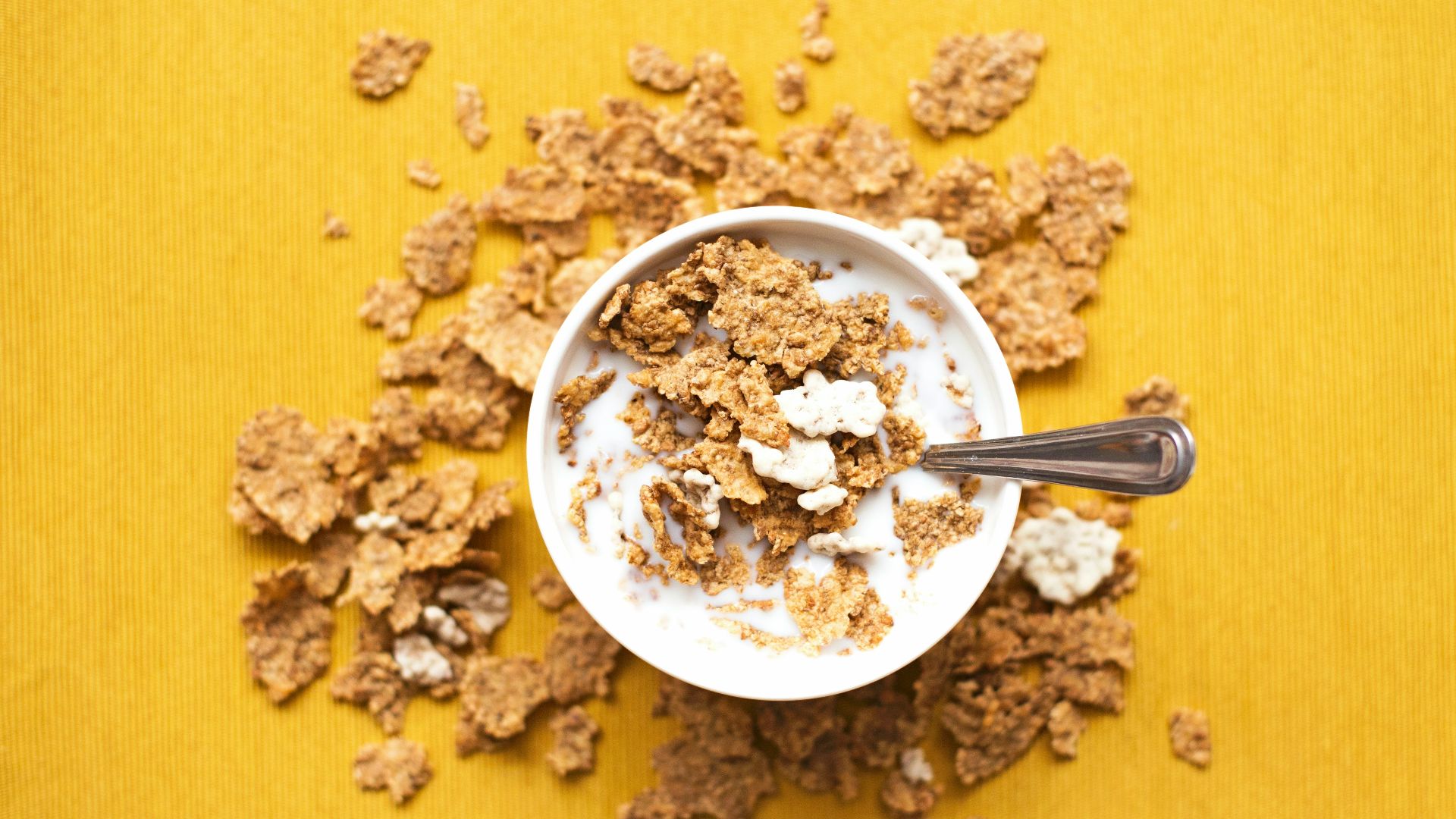 top view of corn flakes in bowl with milk and silver spoon