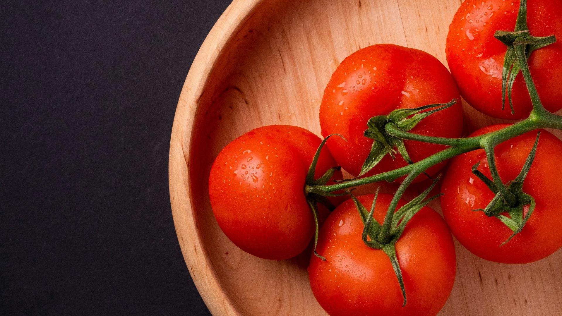five tomatoes in round brown wooden platet