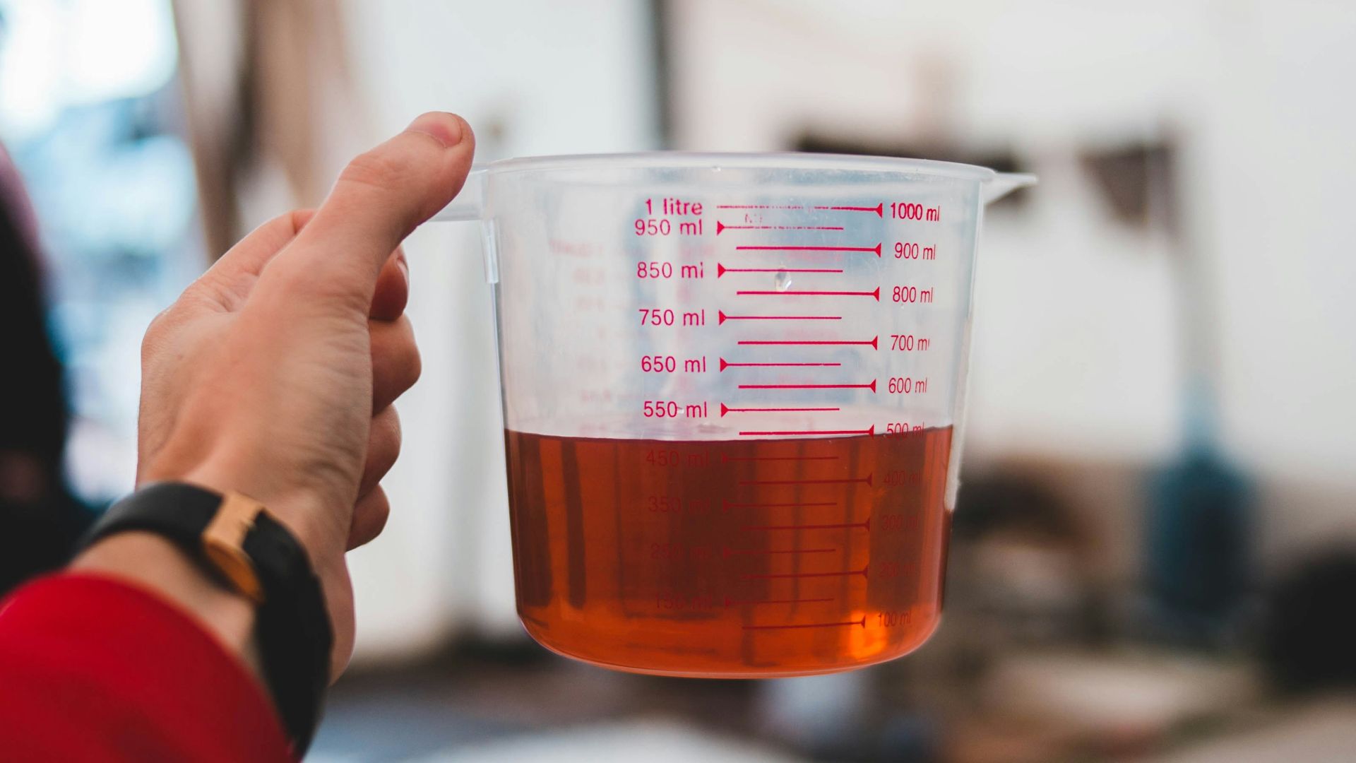 person wearing red long-sleeved top holding plastic measuring pitcher
