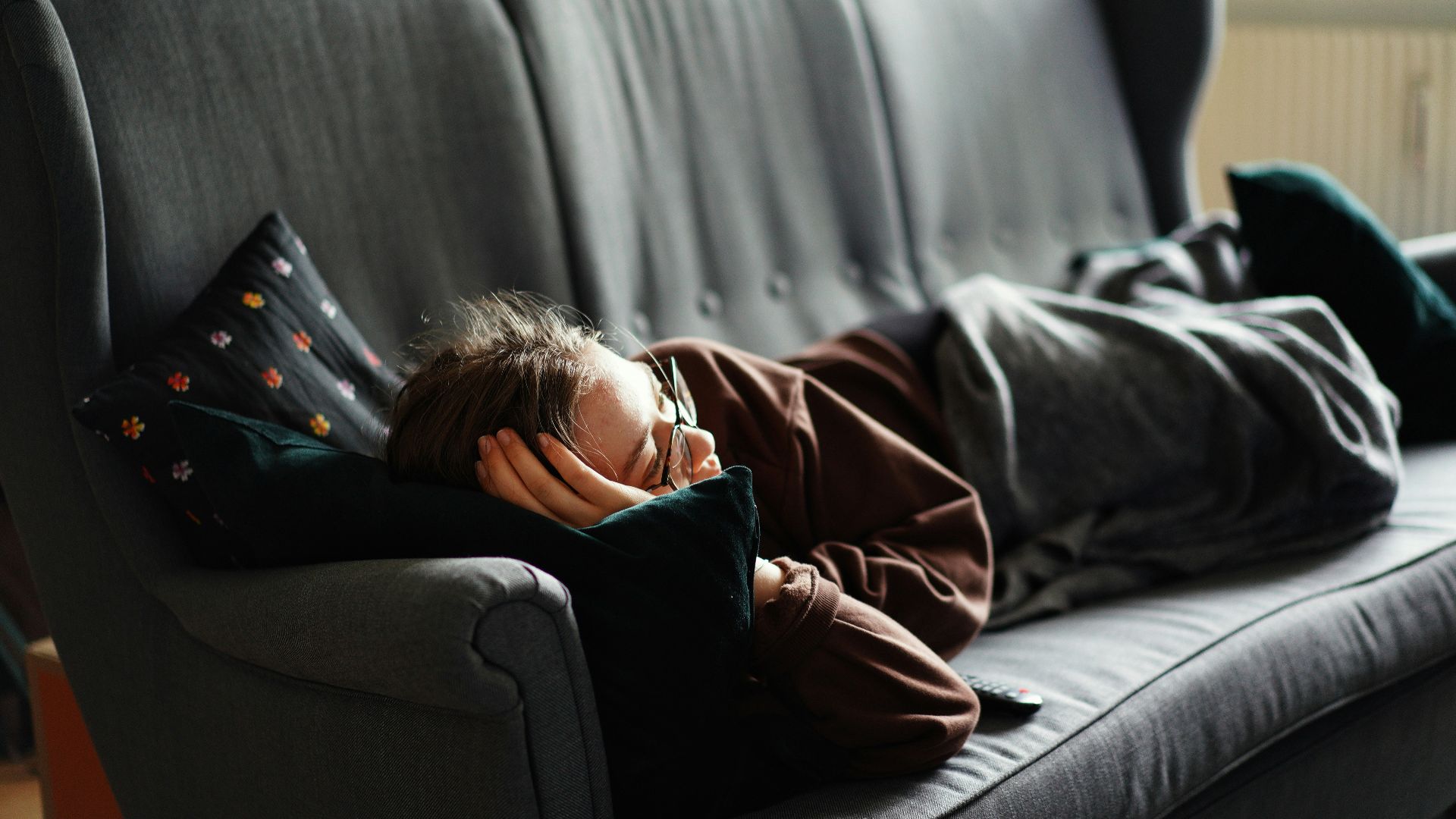 woman in pink jacket lying on gray couch