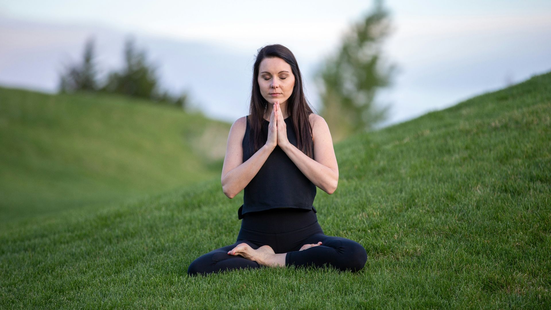 woman in black tank top and black pants sitting on green grass field during daytime