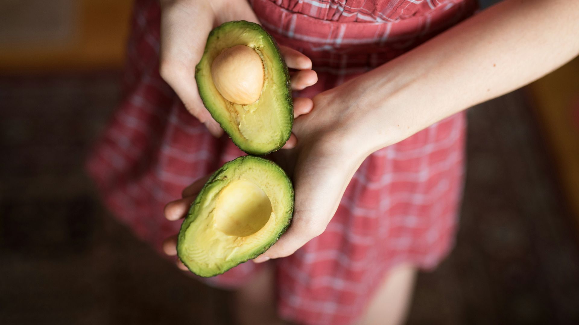 person holding two sliced avocados