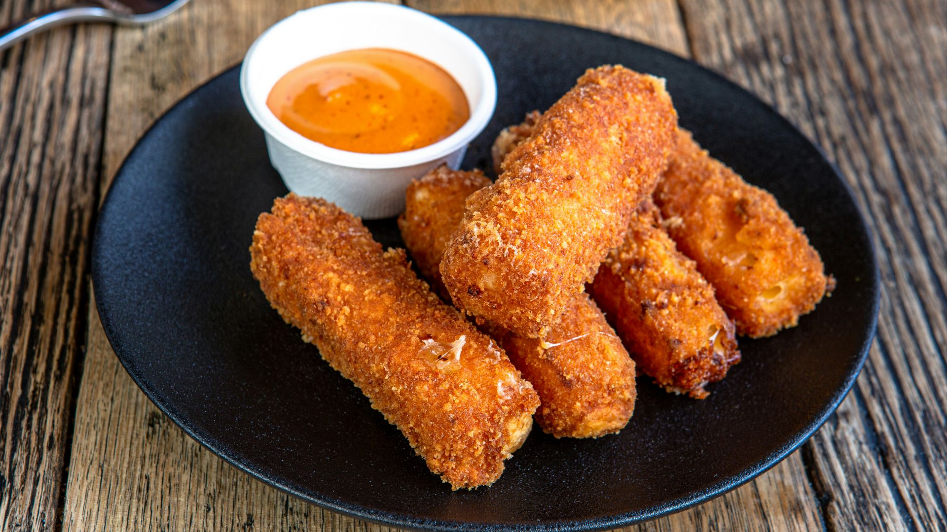 A black plate topped with fried food next to a cup of dipping sauce