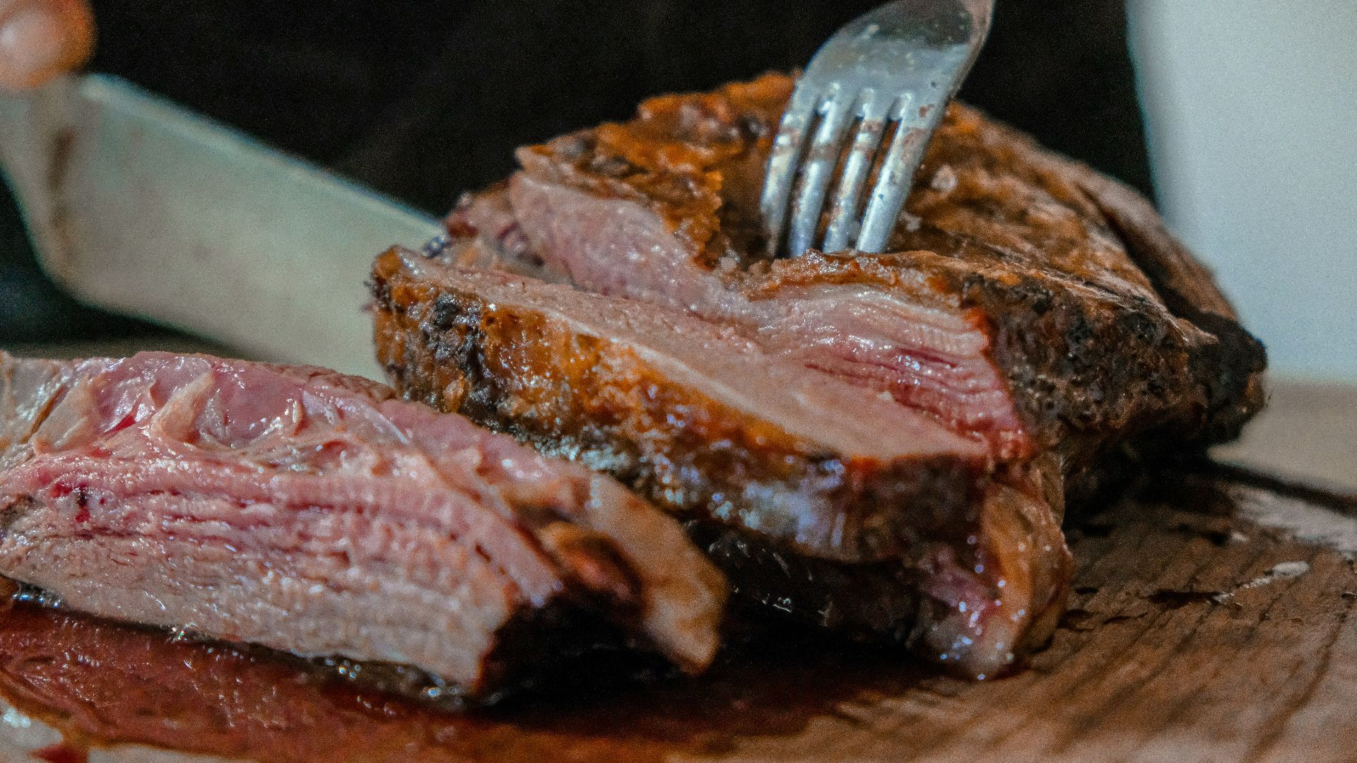 person slicing a meat on brown wooden board