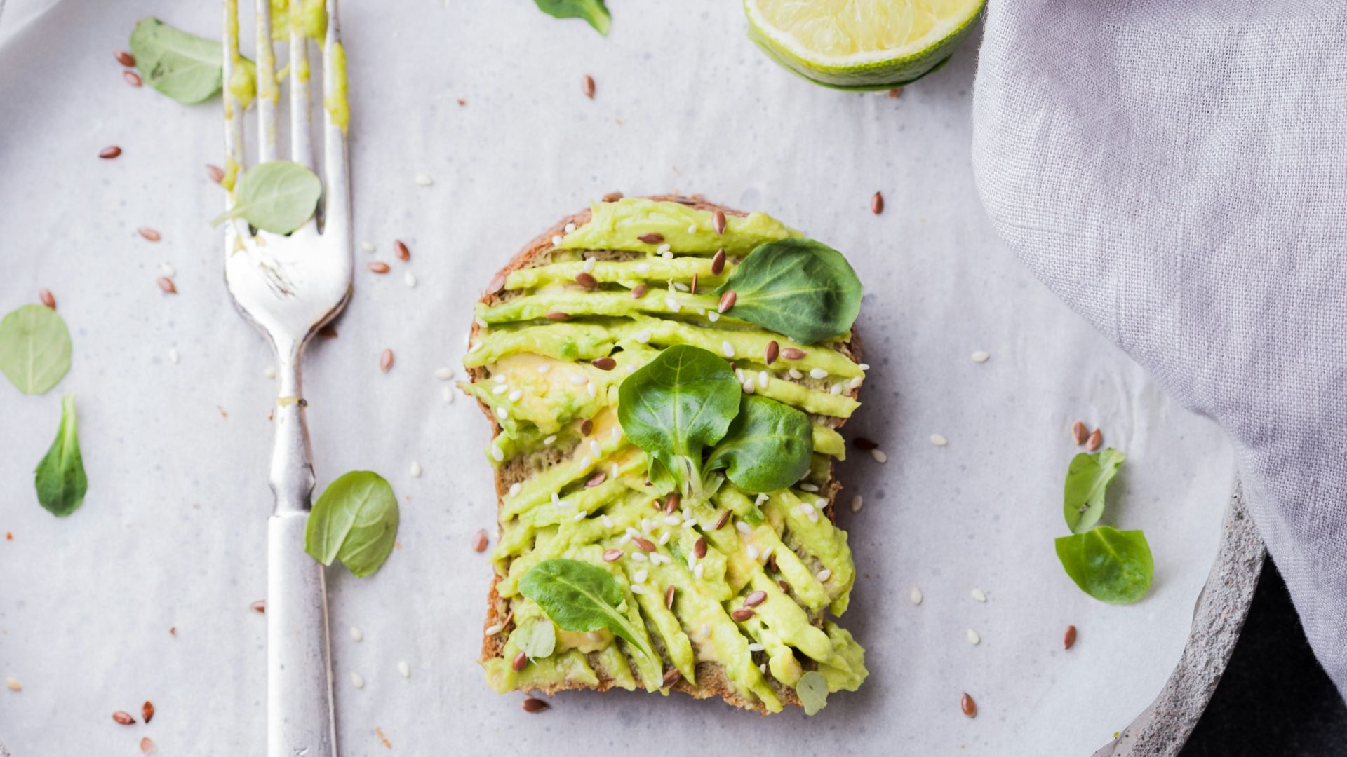 wheat bread with avocado spread beside white plastic spoon and pressed lime on round white plate