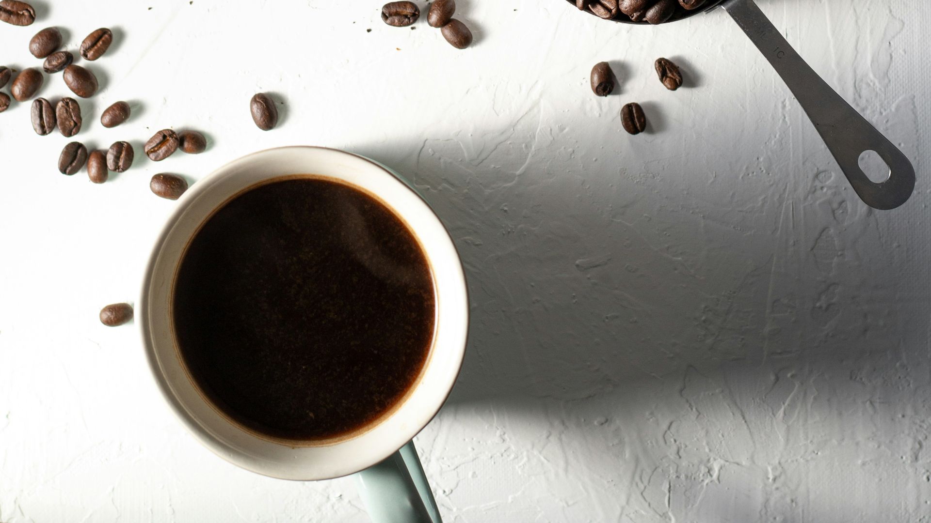 coffee beans on white ceramic mug beside stainless steel spoon