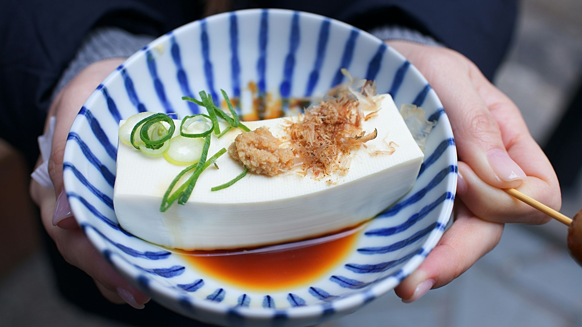 person holding white and blue ceramic plate with rice and sliced cucumber