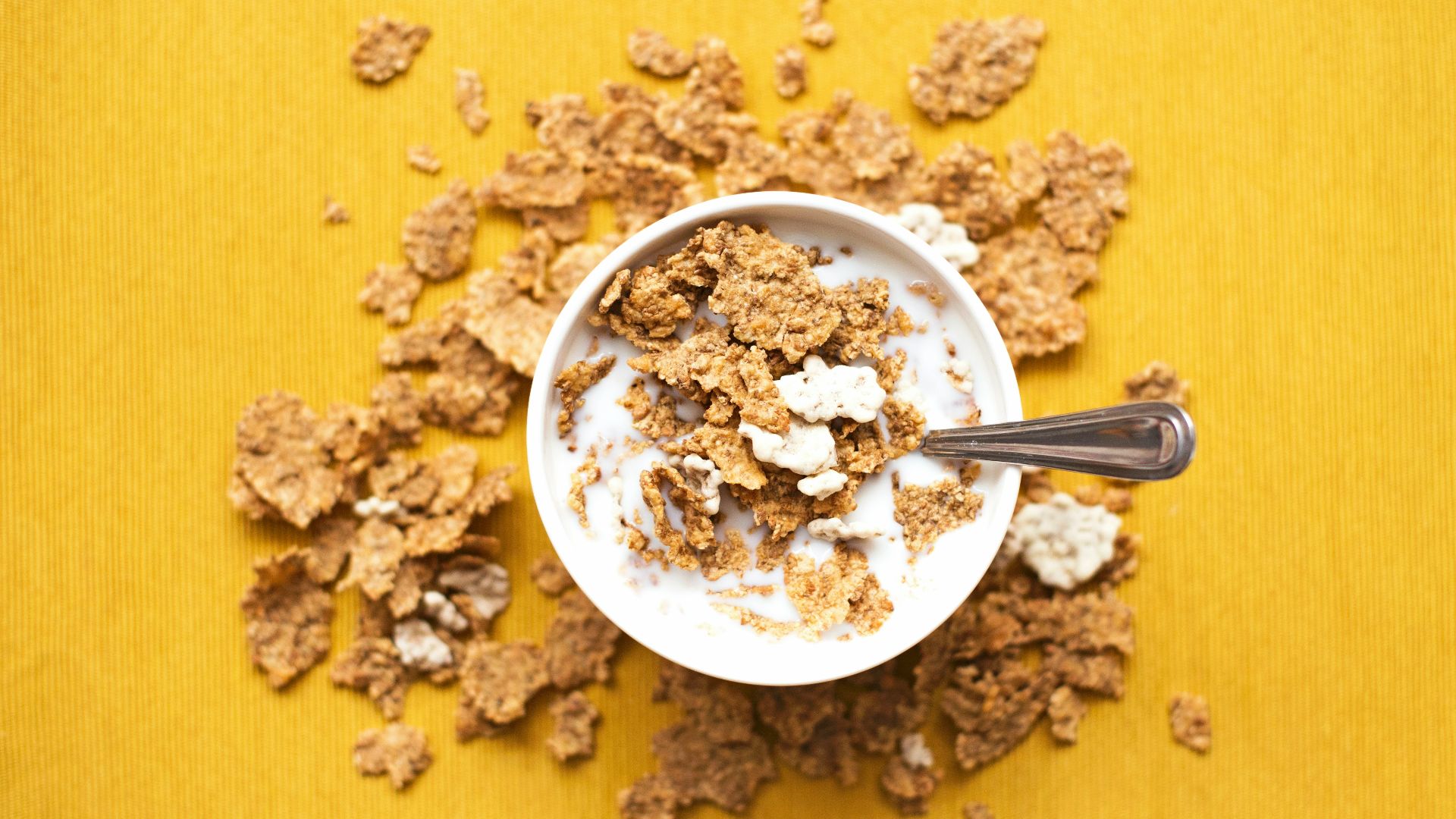 top view of corn flakes in bowl with milk and silver spoon