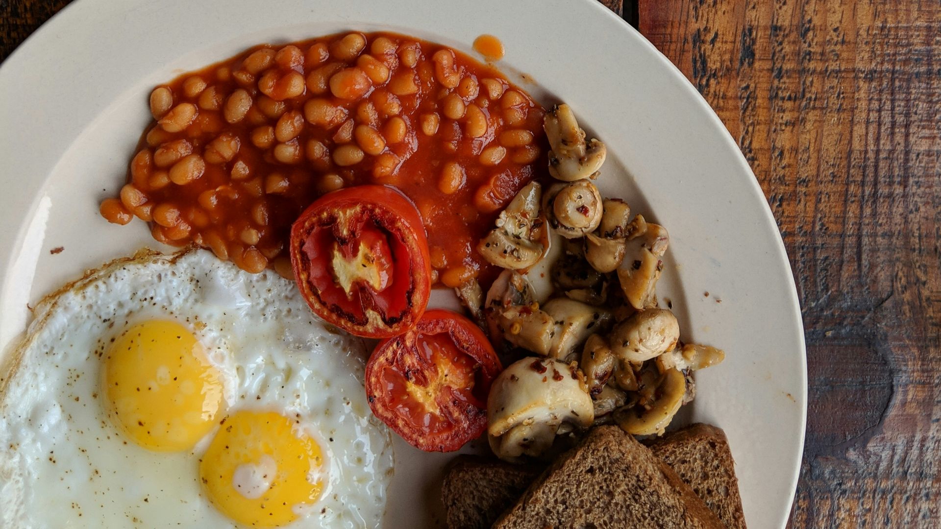 black coffee near sunny side up egg with sliced tomatoes, mushroom and bread on plate