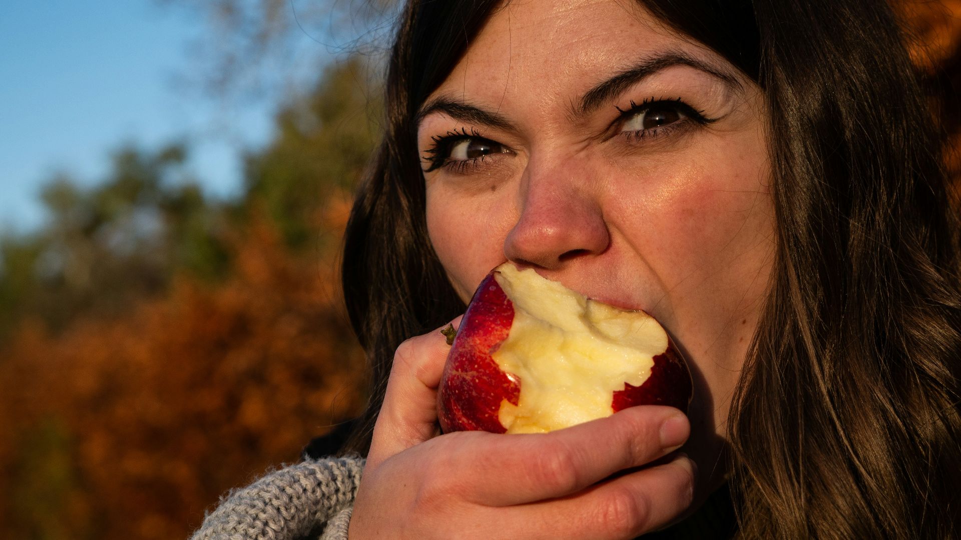 woman in gray sweater holding sliced of apple
