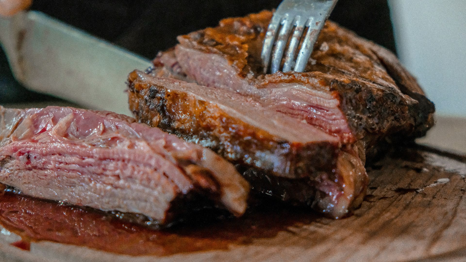 person slicing a meat on brown wooden board