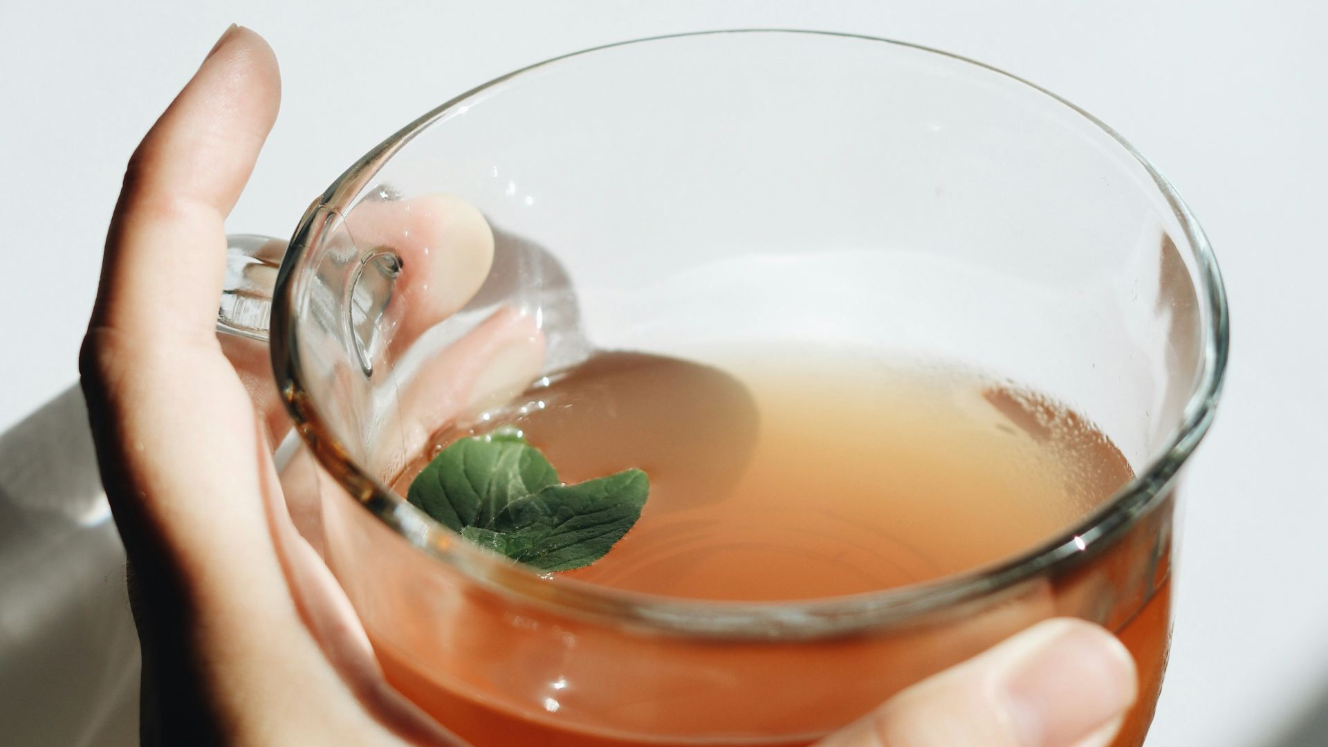 person holding clear drinking glass with brown liquid