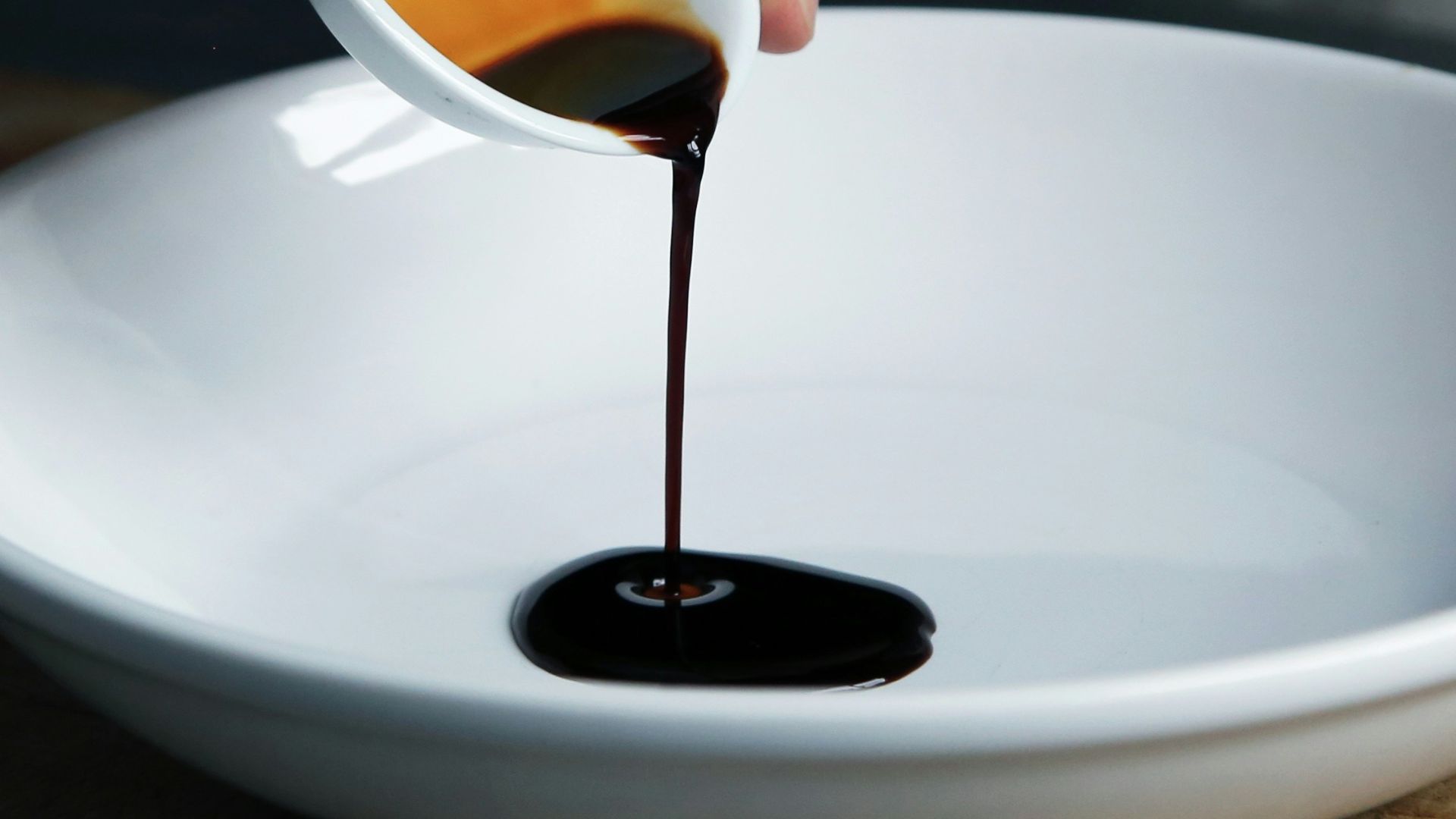 person dripping black liquid from small white ceramic bowl to big white ceramic bowl