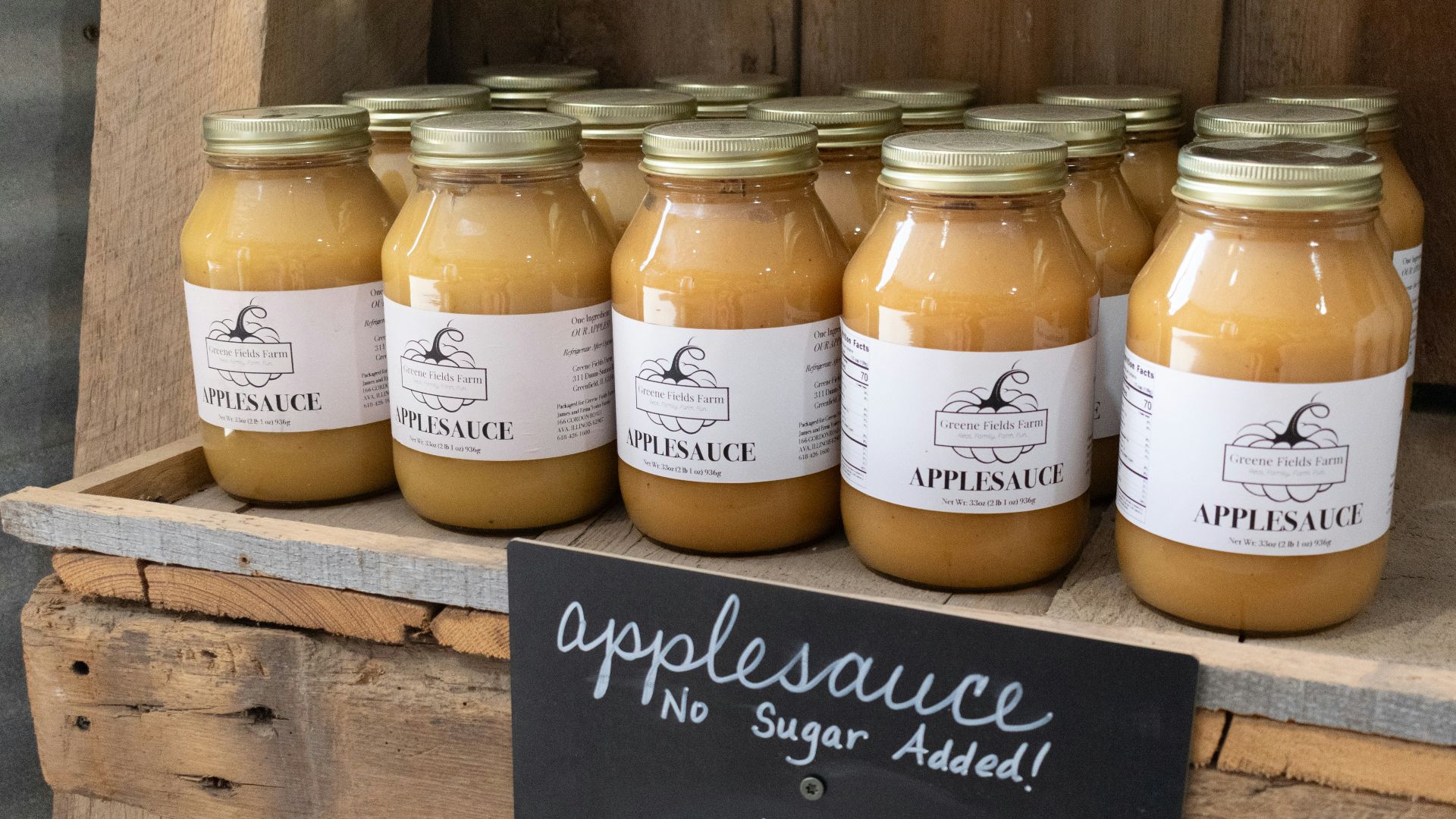 Jars of applesauce sit on a wooden shelf.