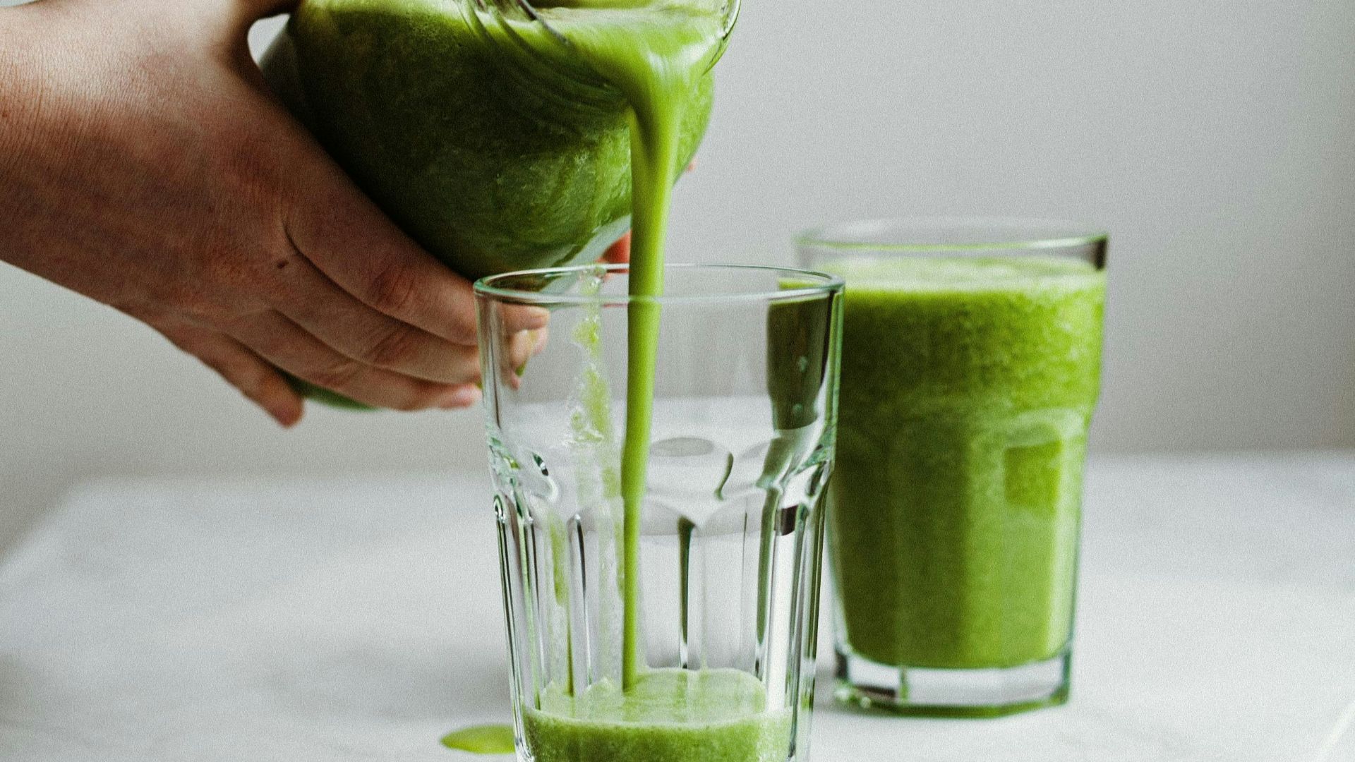 person holding clear drinking glass with green liquid