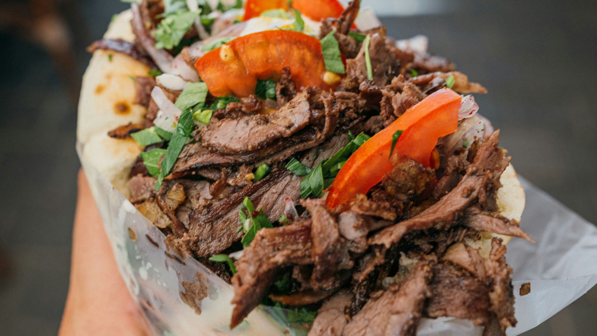 a person holding a sandwich with meat and vegetables