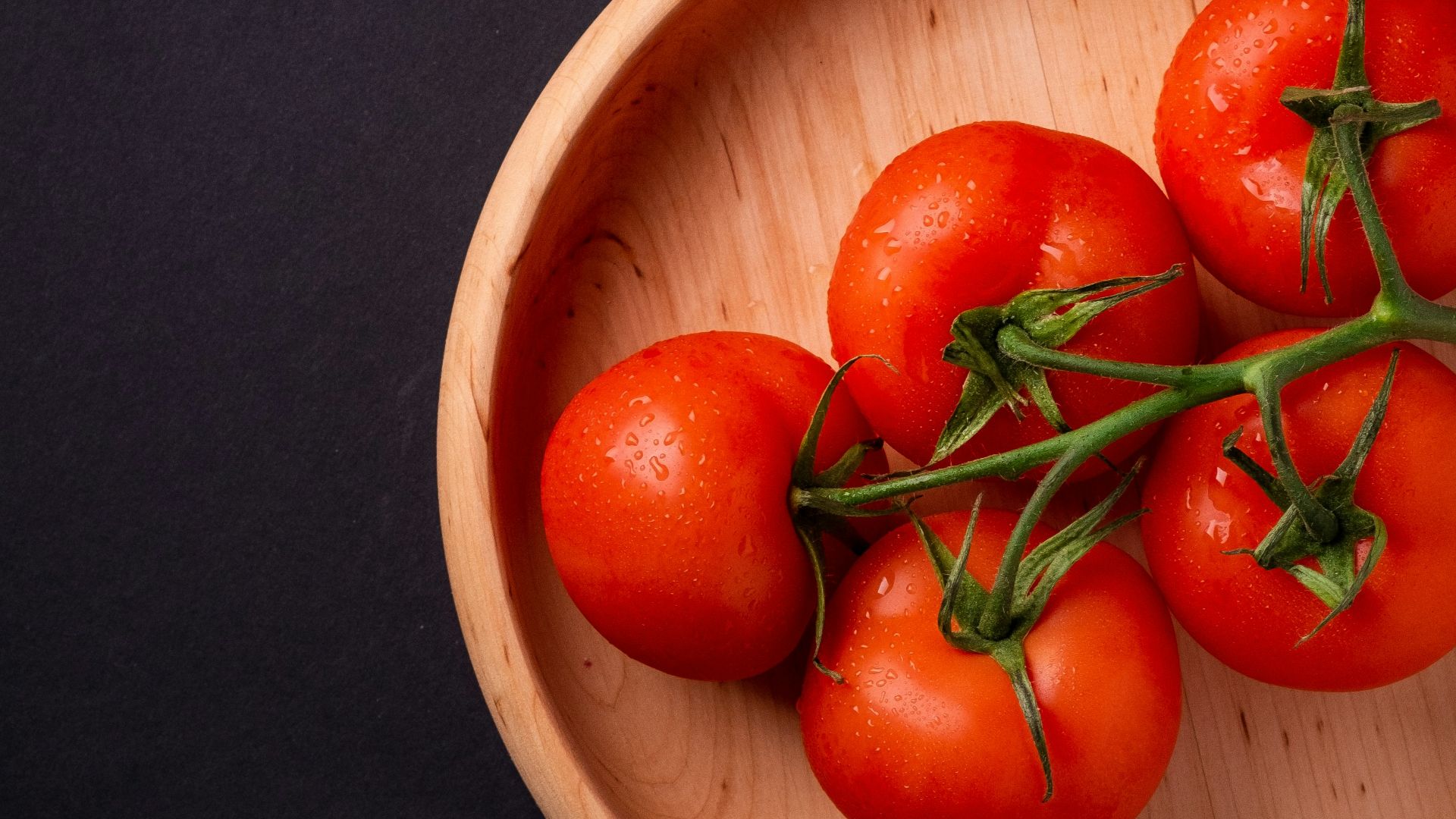 five tomatoes in round brown wooden platet