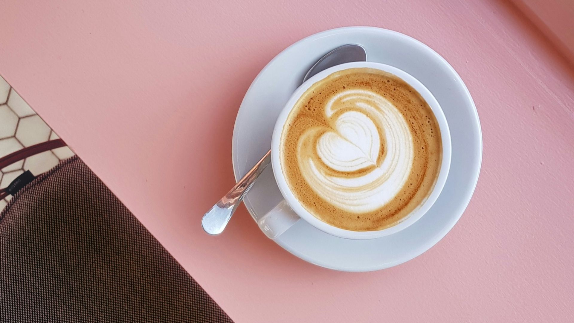 cup of coffee on saucer with teaspoon on pink tabletop