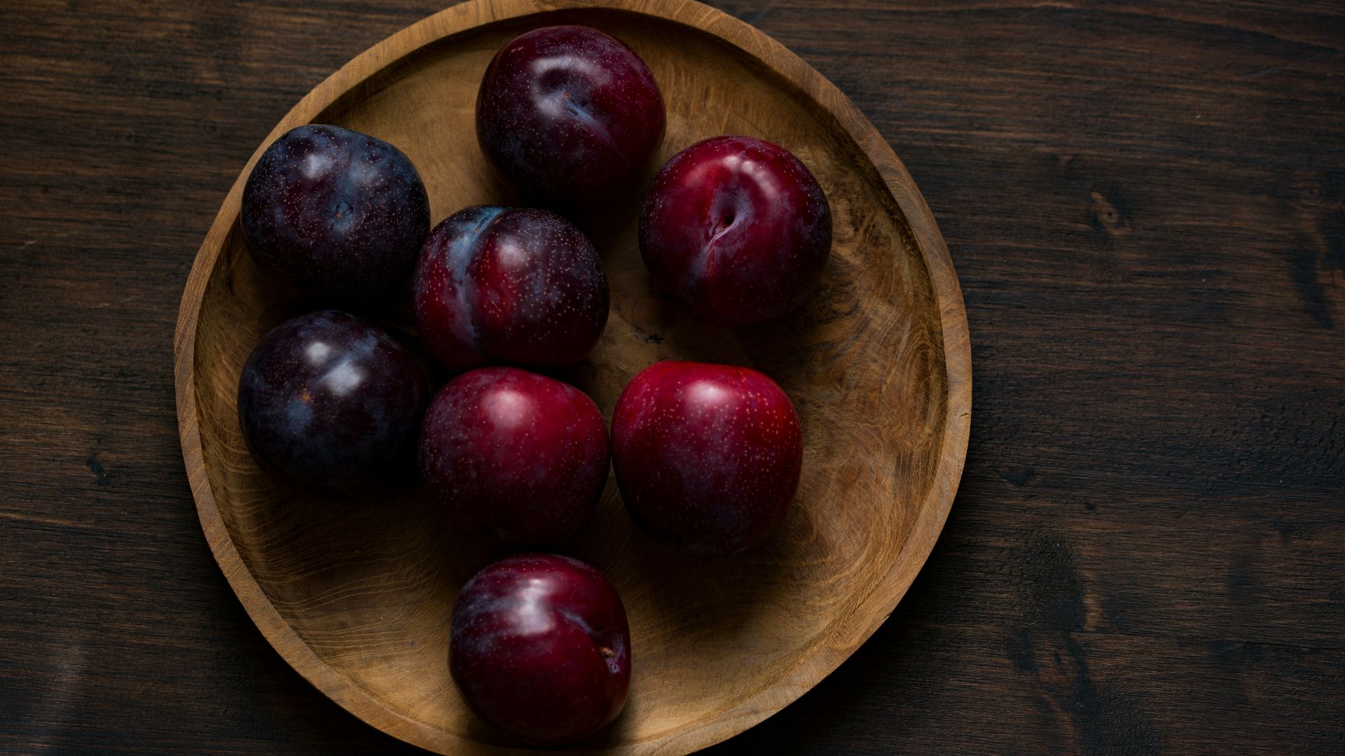 red plum fruits on round brown wooden plate