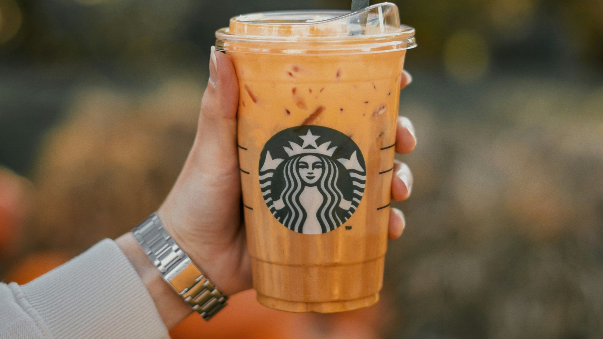 a person holding a starbucks drink with oranges in the background