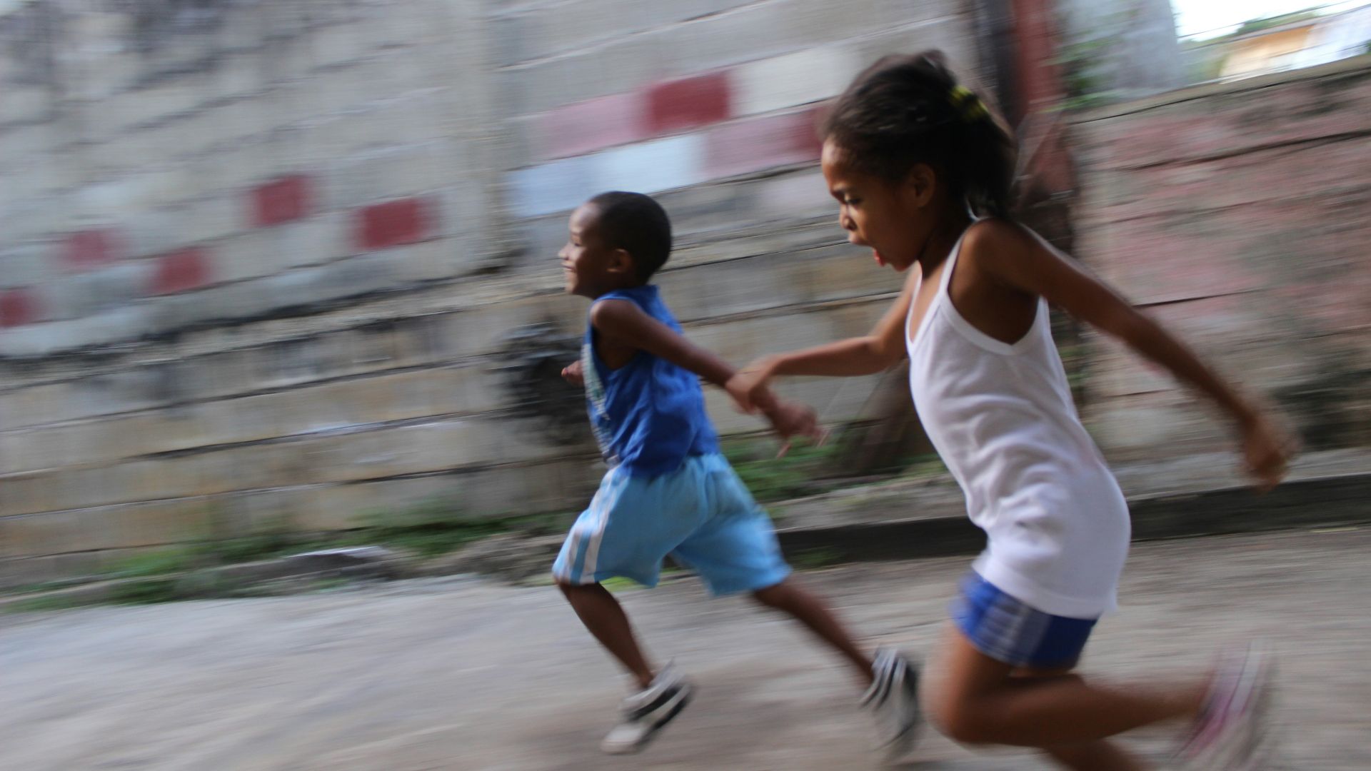 two girl and boy running beside gray wall