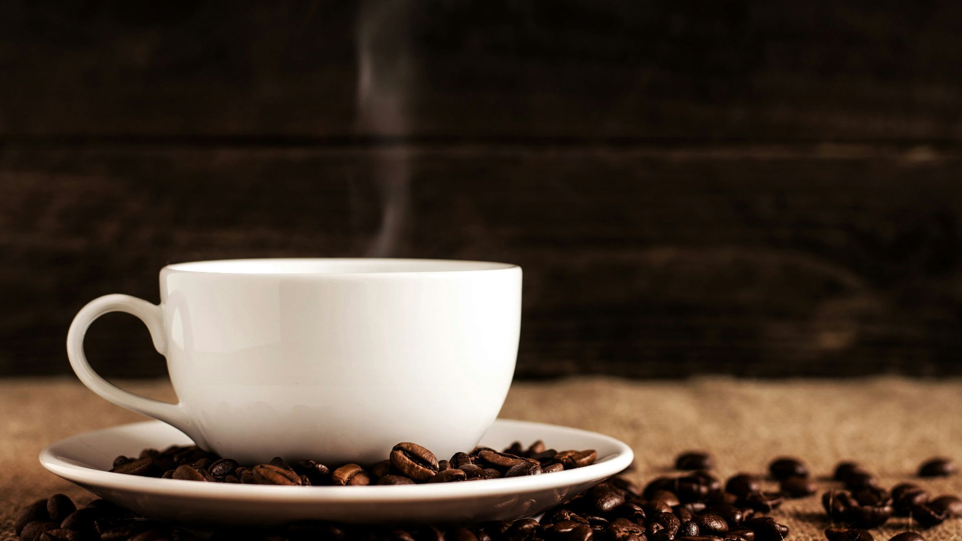 white ceramic mug and saucer with coffee beans on brown textile