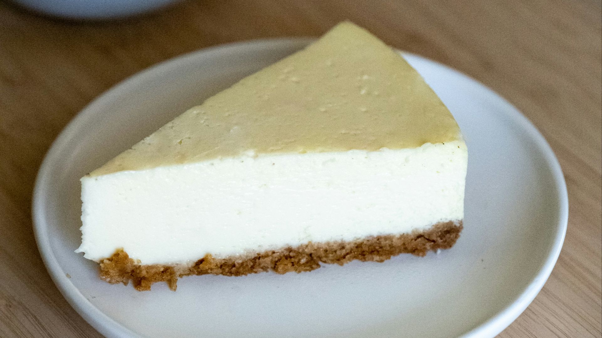 a piece of cheesecake on a plate next to a cup of tea