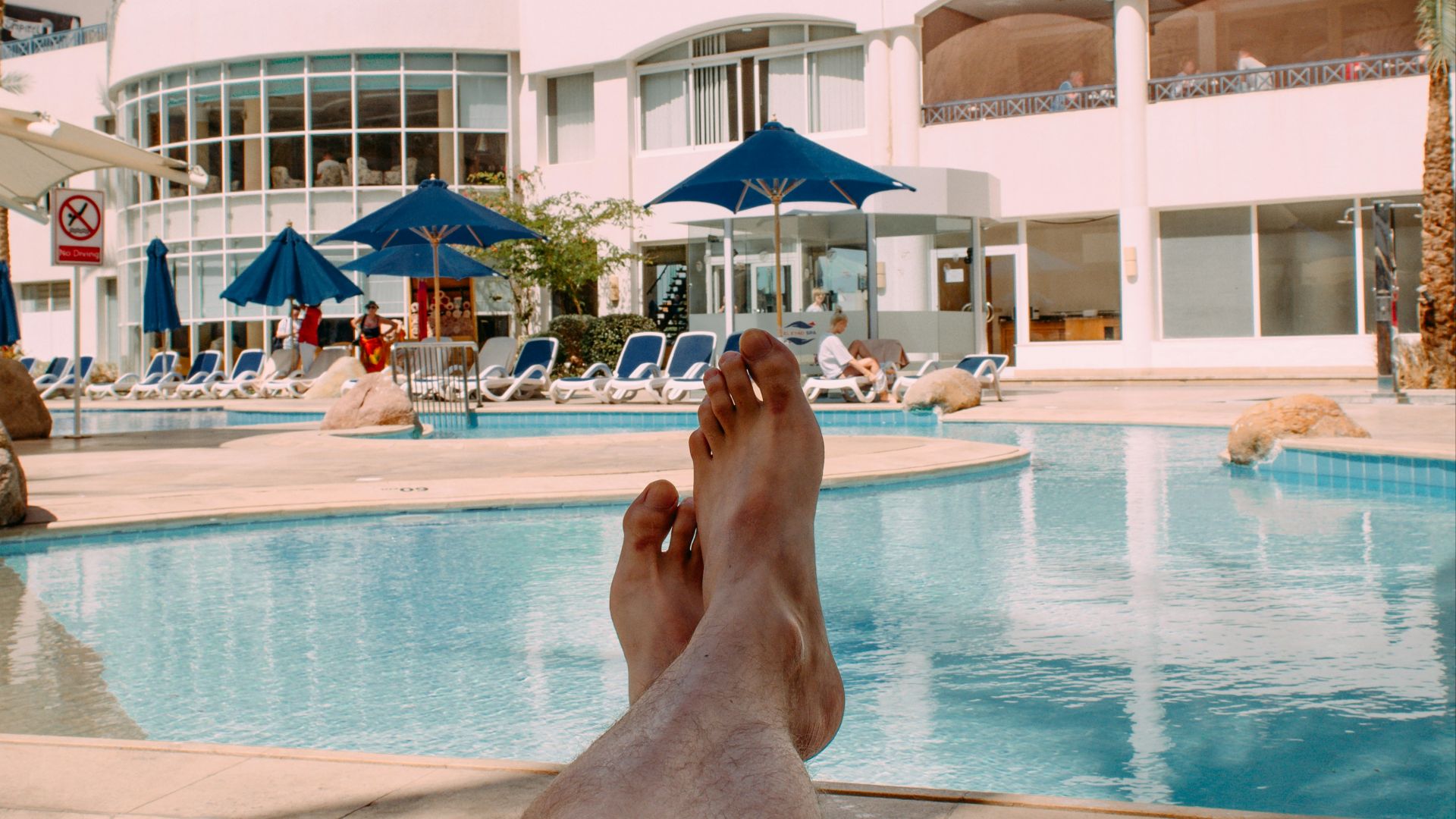 person in black shorts lying on blue and white stripe bed near swimming pool during daytime