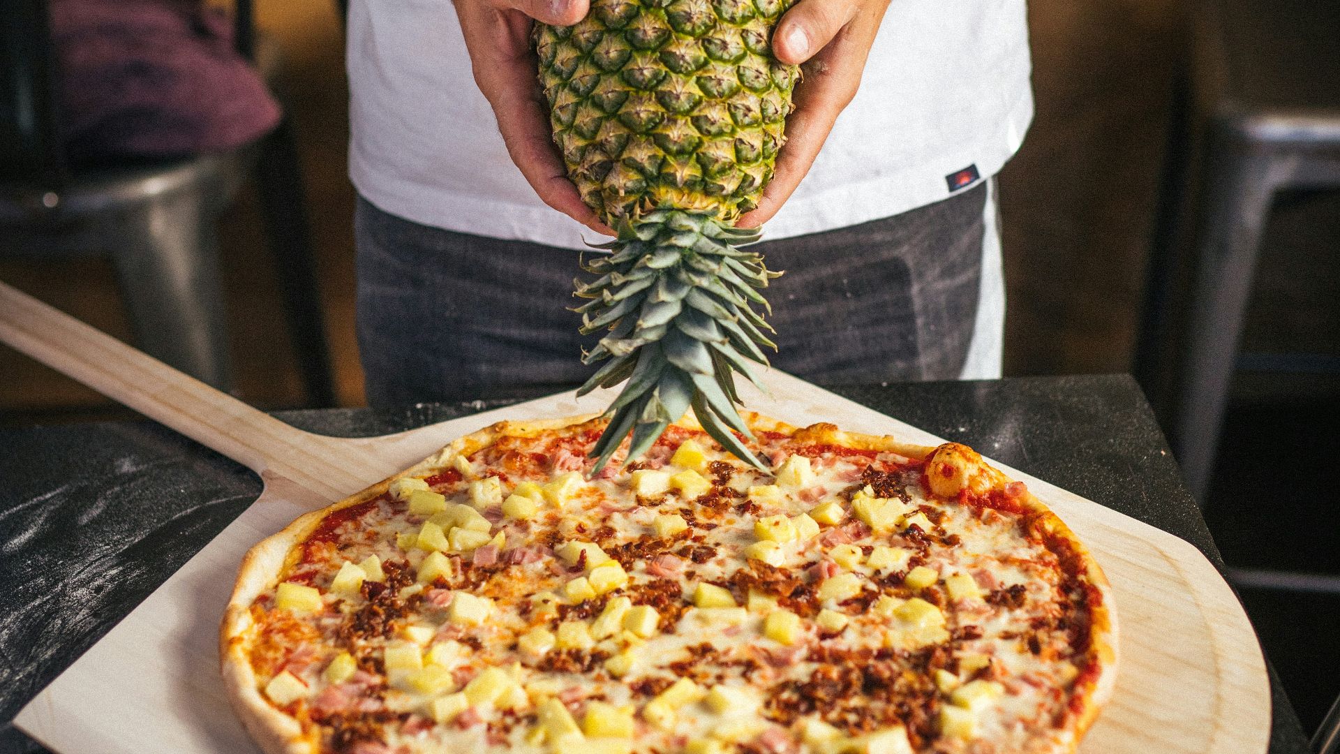a man holding a pineapple on top of a pizza