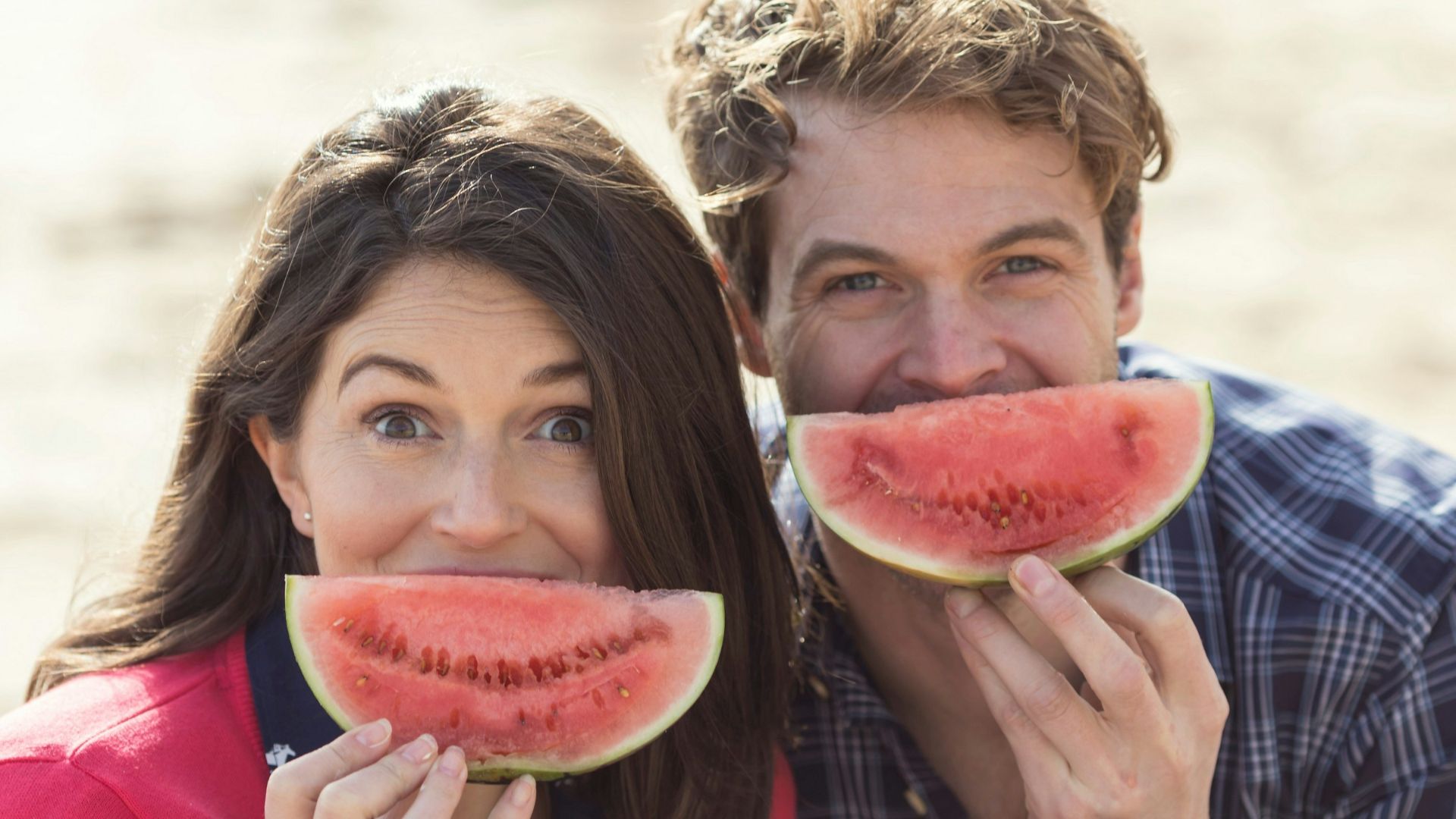 a man and a woman eating watermelon on the beach