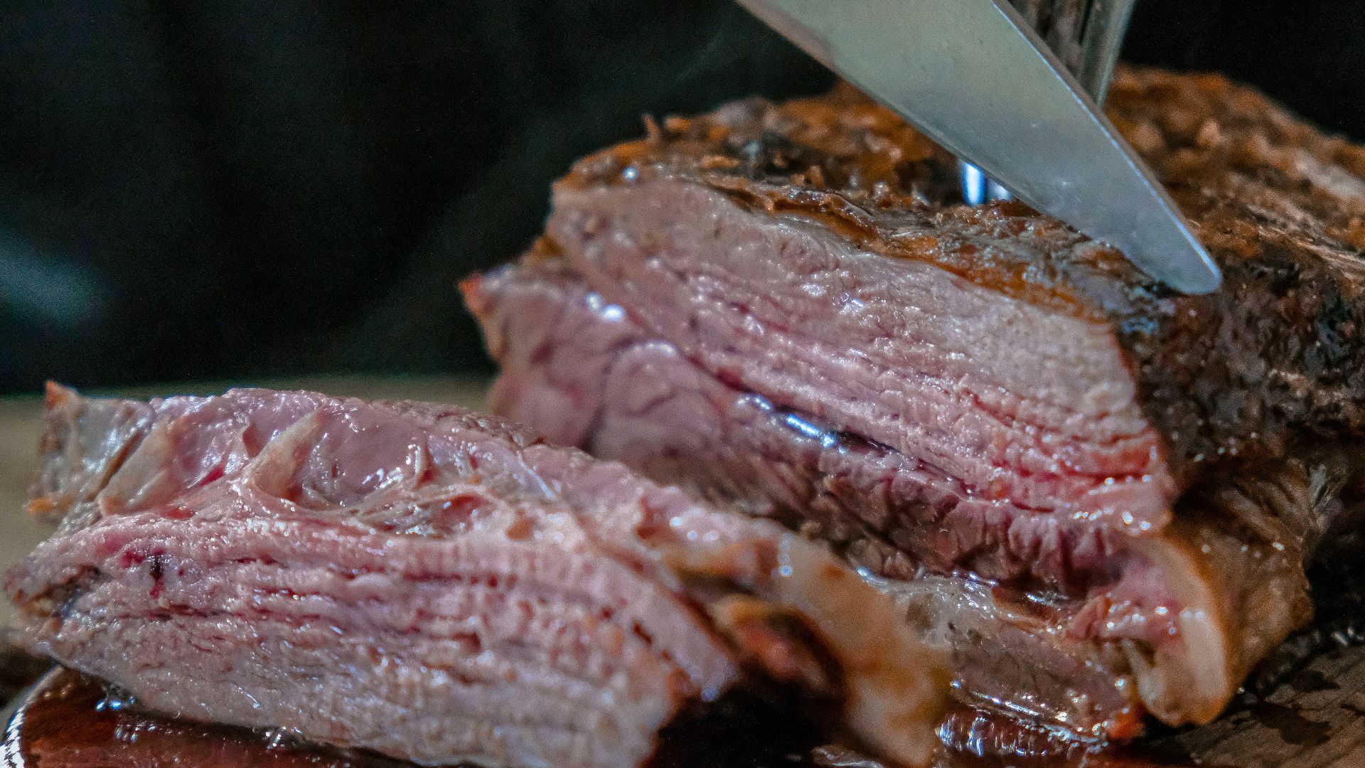 person slicing juicy medium rare meat on top of brown wooden cutting board