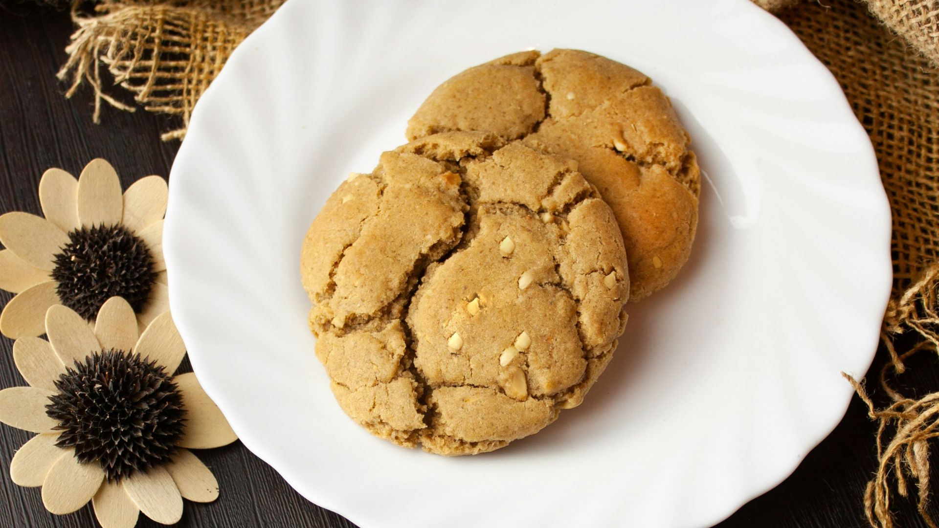 two cookies on a white plate next to dried flowers